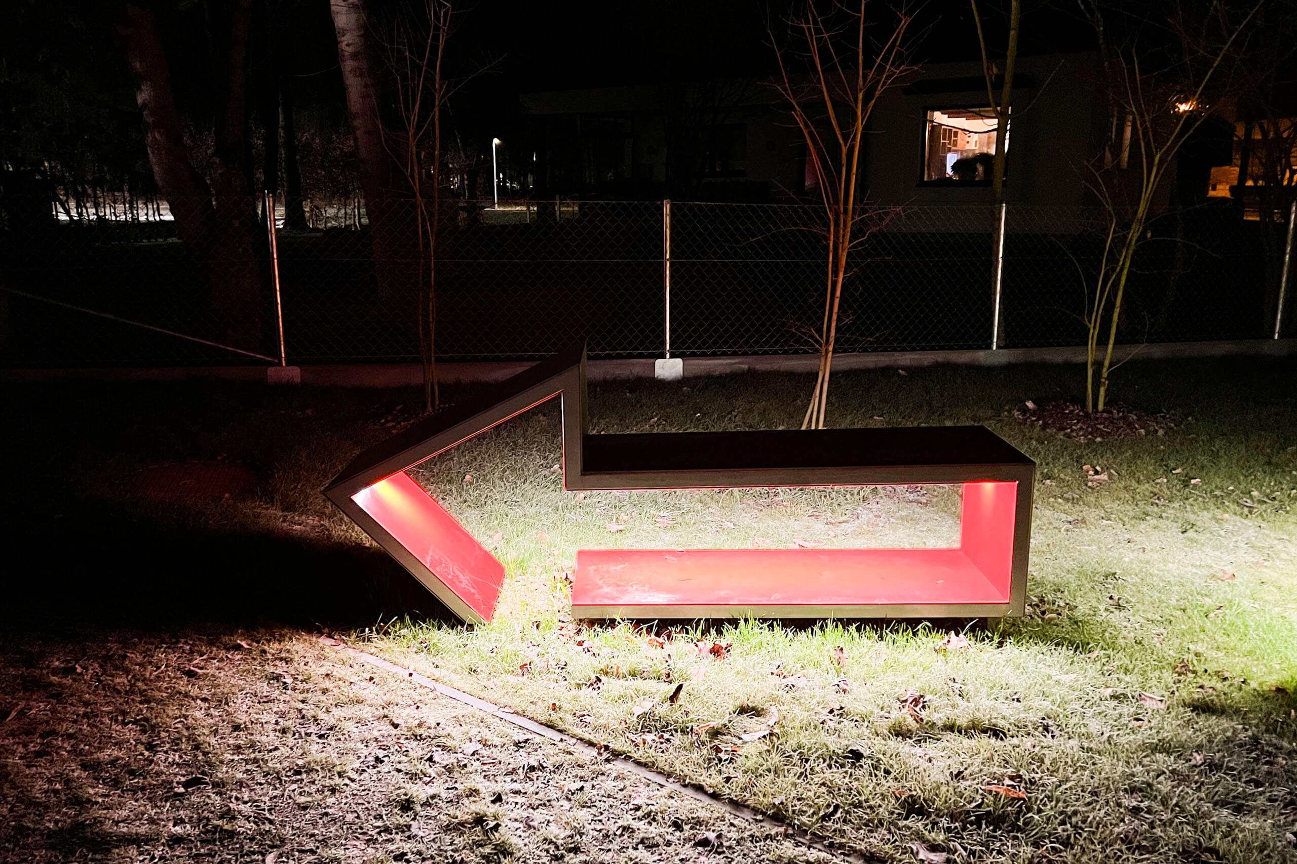 Pfeilförmige Sitzbank mit roter Innenbeleuchtung im Außenbereich bei Nacht