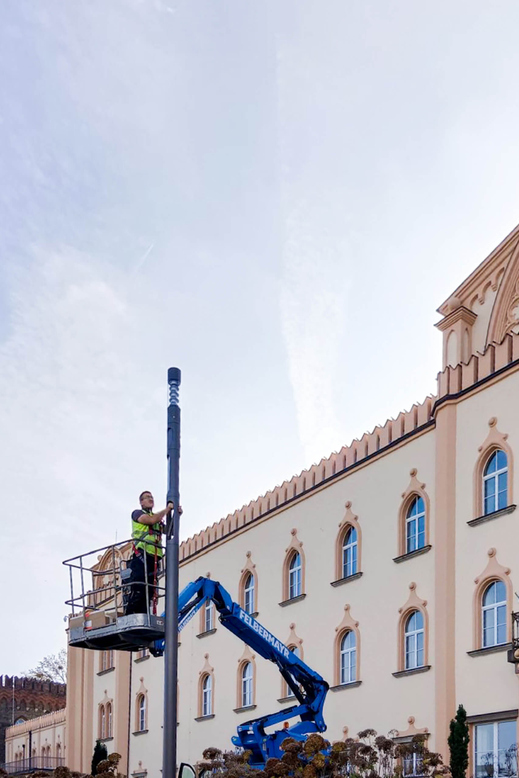 Ein Arbeiter in einem Hubsteiger installiert eine Straßenlaterne vor einem Gebäude.