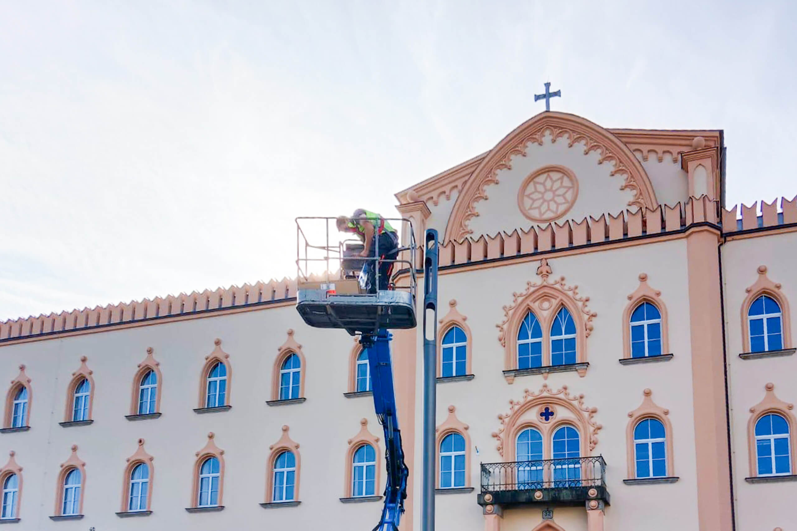 Mann in Hebebühne reinigt Fassade eines historischen Gebäudes.