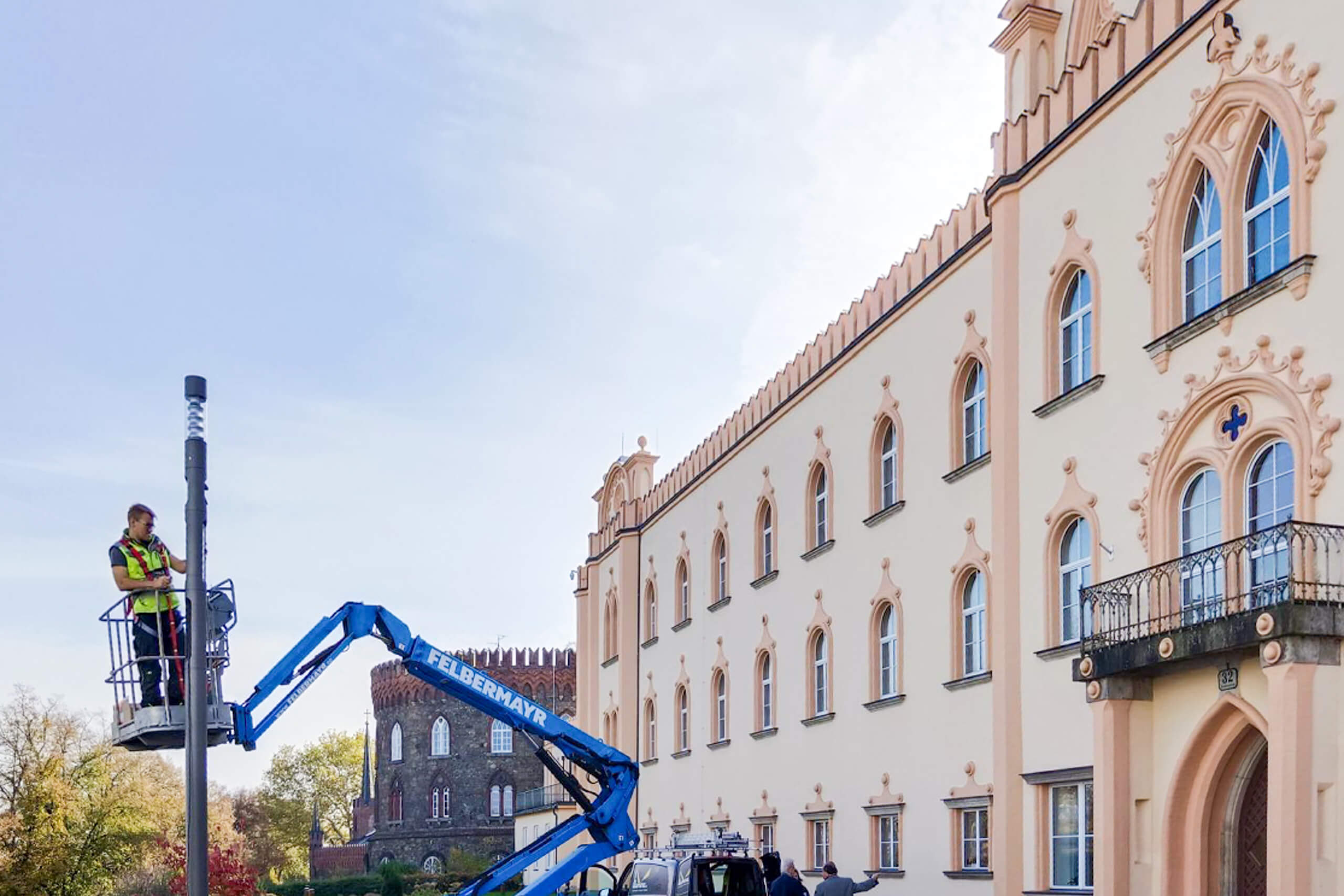 Arbeiter in Arbeitsbühne installiert Leuchte vor historischem Gebäude