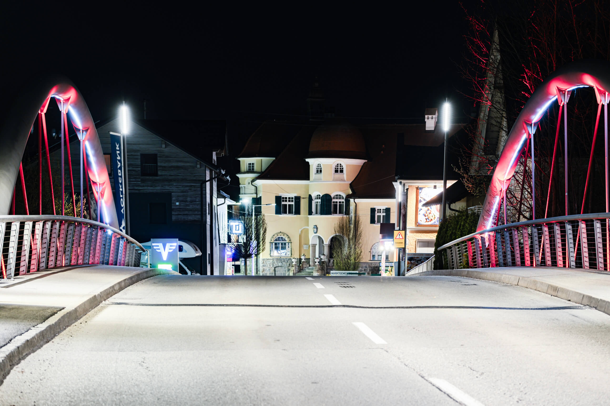 Beleuchtete Brücke mit roten Bögen und Gebäuden bei Nacht