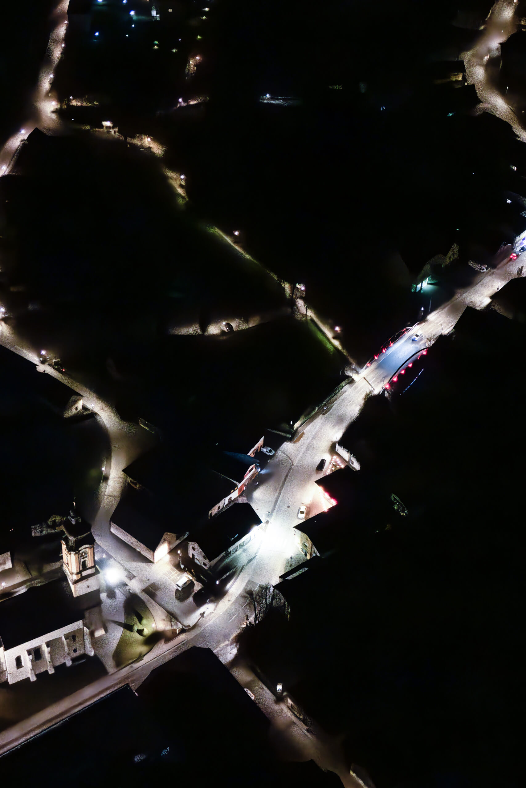 Luftaufnahme einer beleuchteten Brücke und Dorfkirche bei Nacht