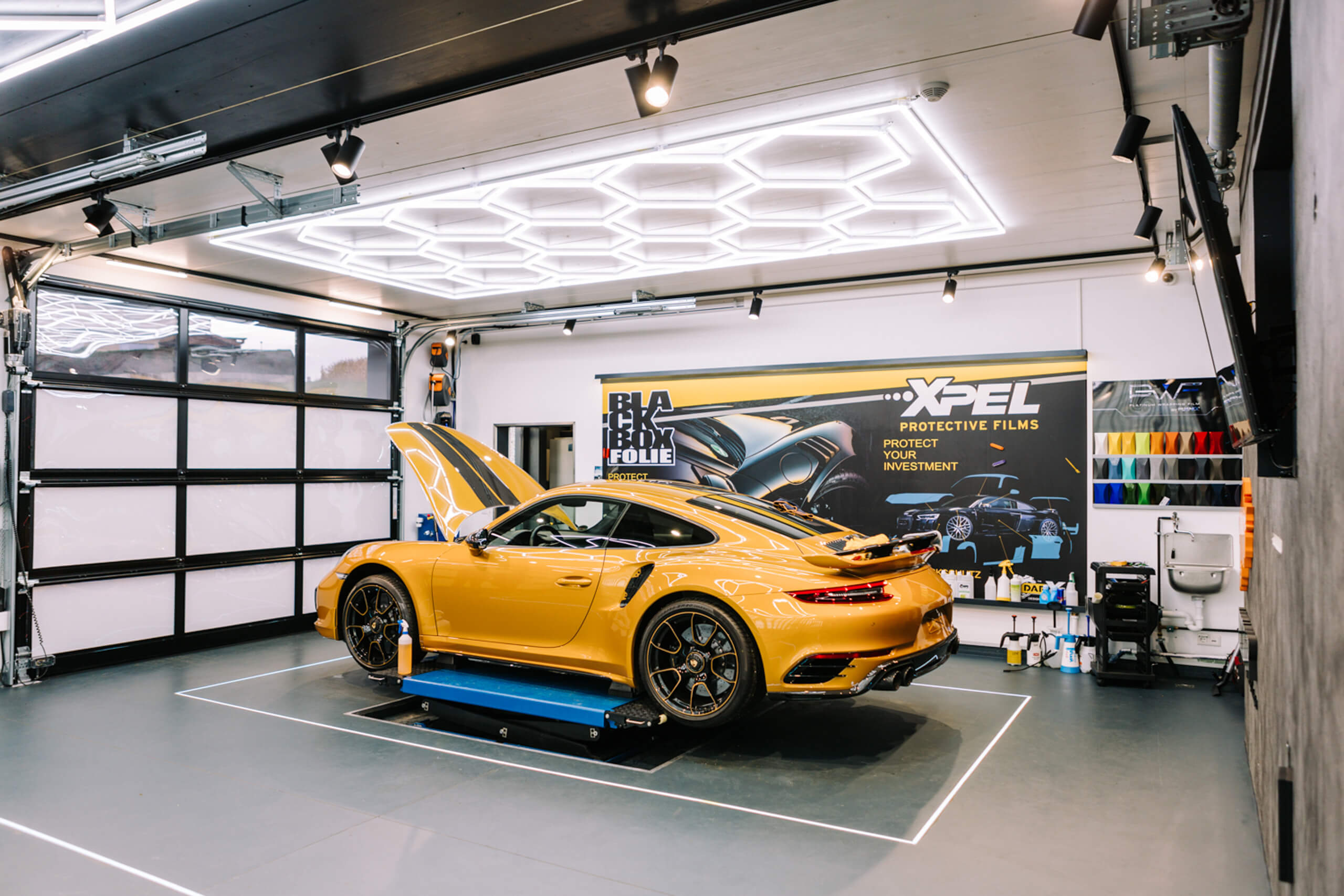 Porsche 911 Turbo S in gelber Lackierung mit geöffneter Motorhaube in einem modernen Showroom mit LED-Beleuchtung