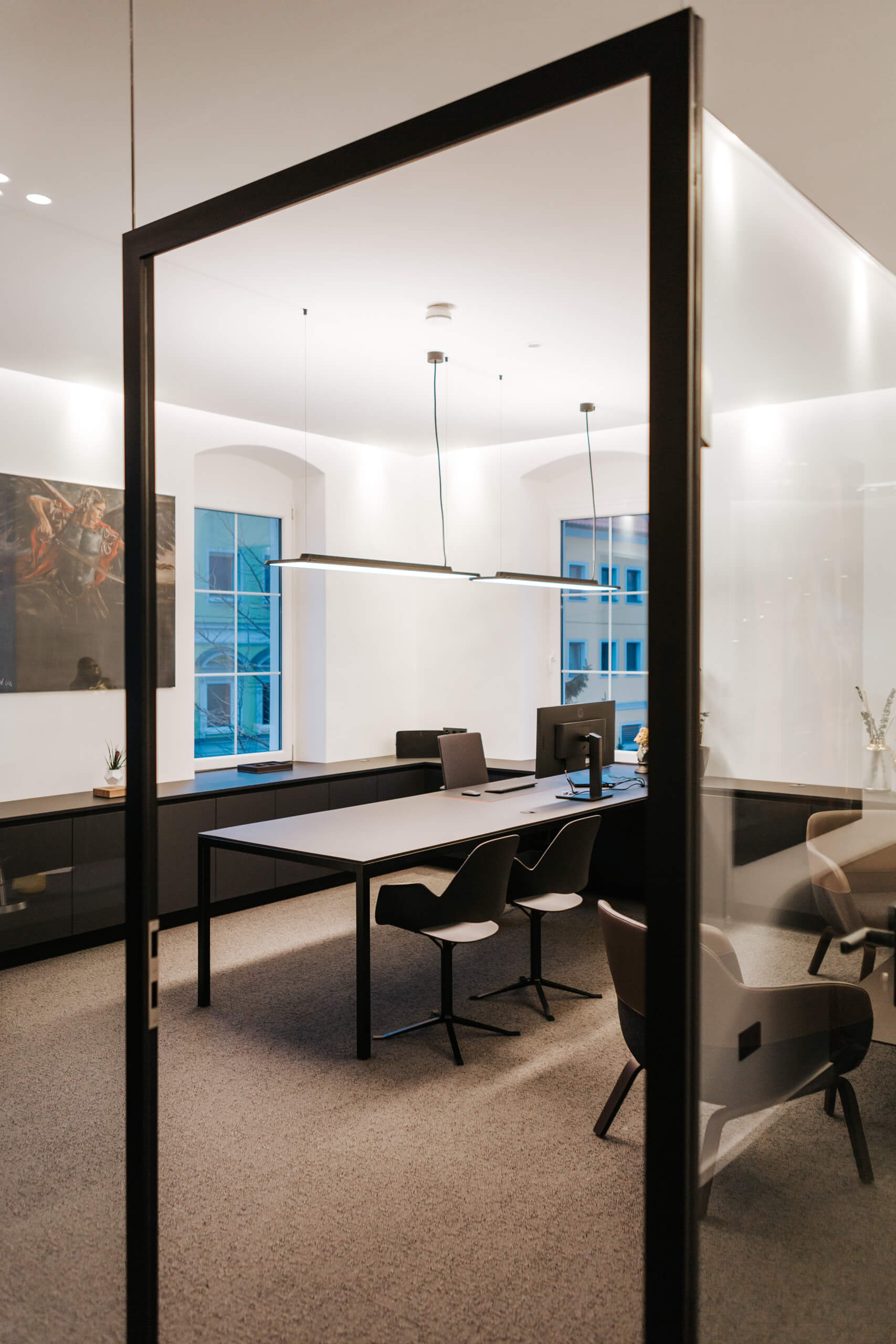 Modernes Büro mit Schreibtischen und Stühlen, beleuchtet durch lineare Pendelleuchten.