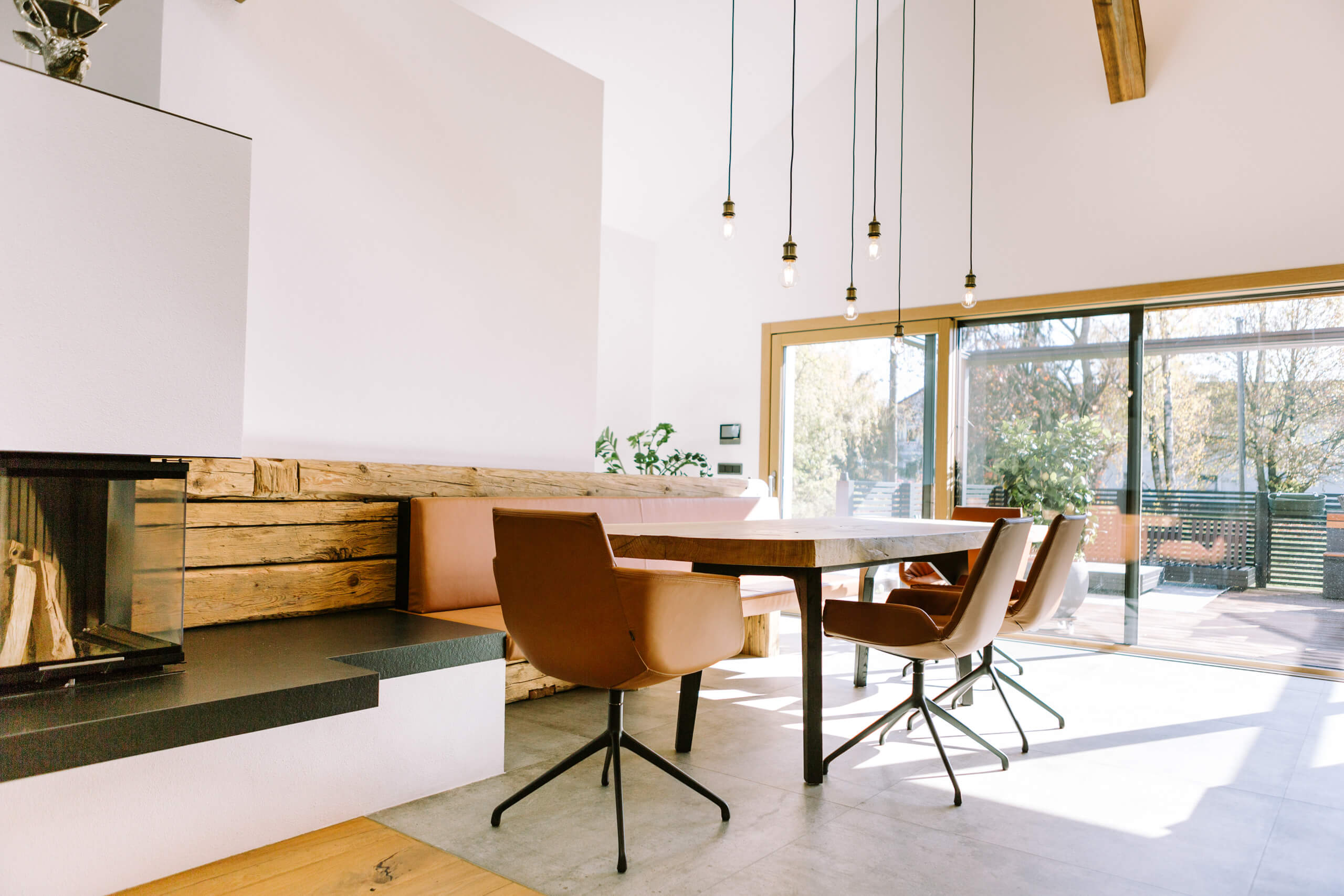 Modernes Esszimmer mit Holztisch, Ledersesseln und Kamin – Lichtplanung von Illumina.