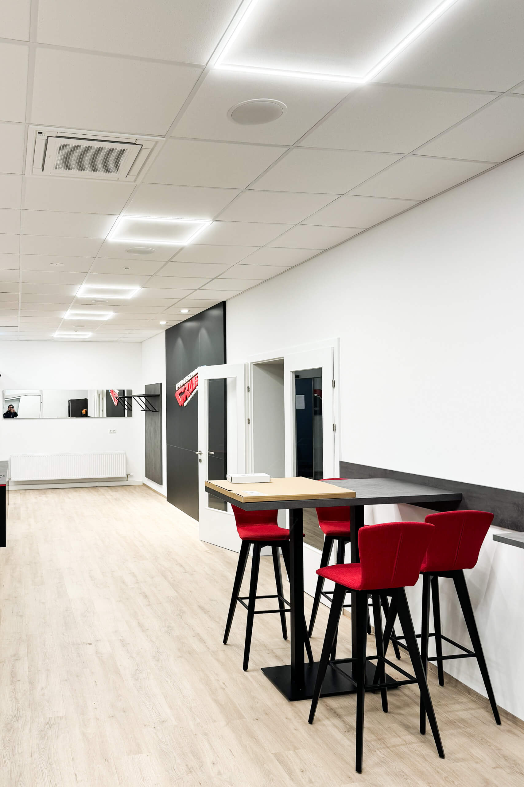 Moderne Büroeinrichtung mit Stehtisch und roten Barhockern – Lichtplanung von Illumina.