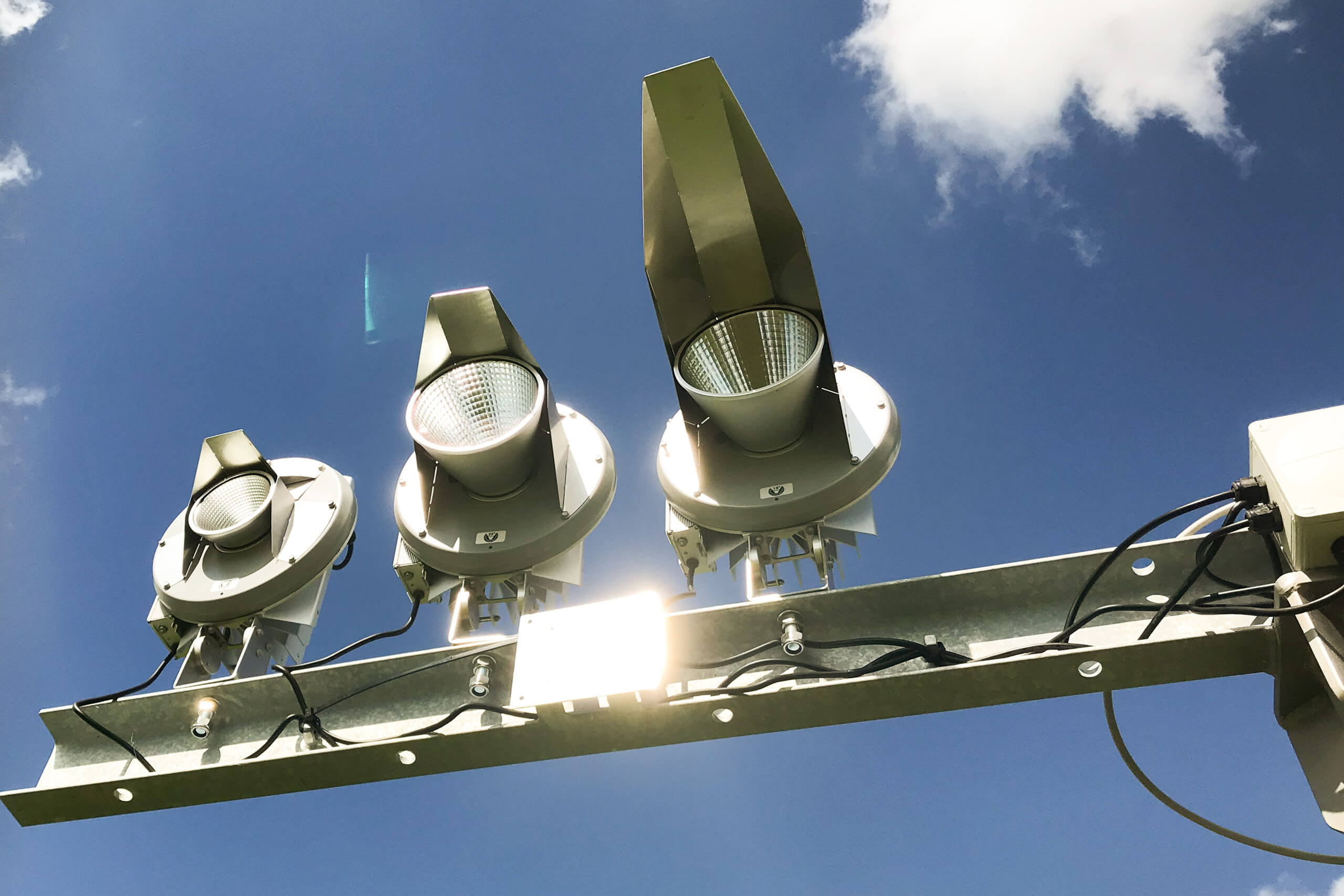 Drei moderne LED-Straßenleuchten an einem Mast im Freien bei Tageslicht.