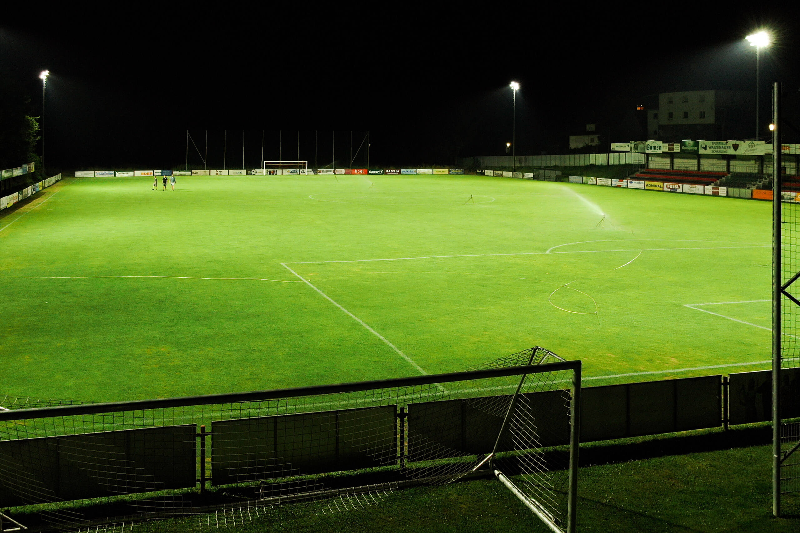 Fußballplatz bei Nacht mit Sprinkleranlage und Flutlicht – Sportplatzbeleuchtung von Illumina.