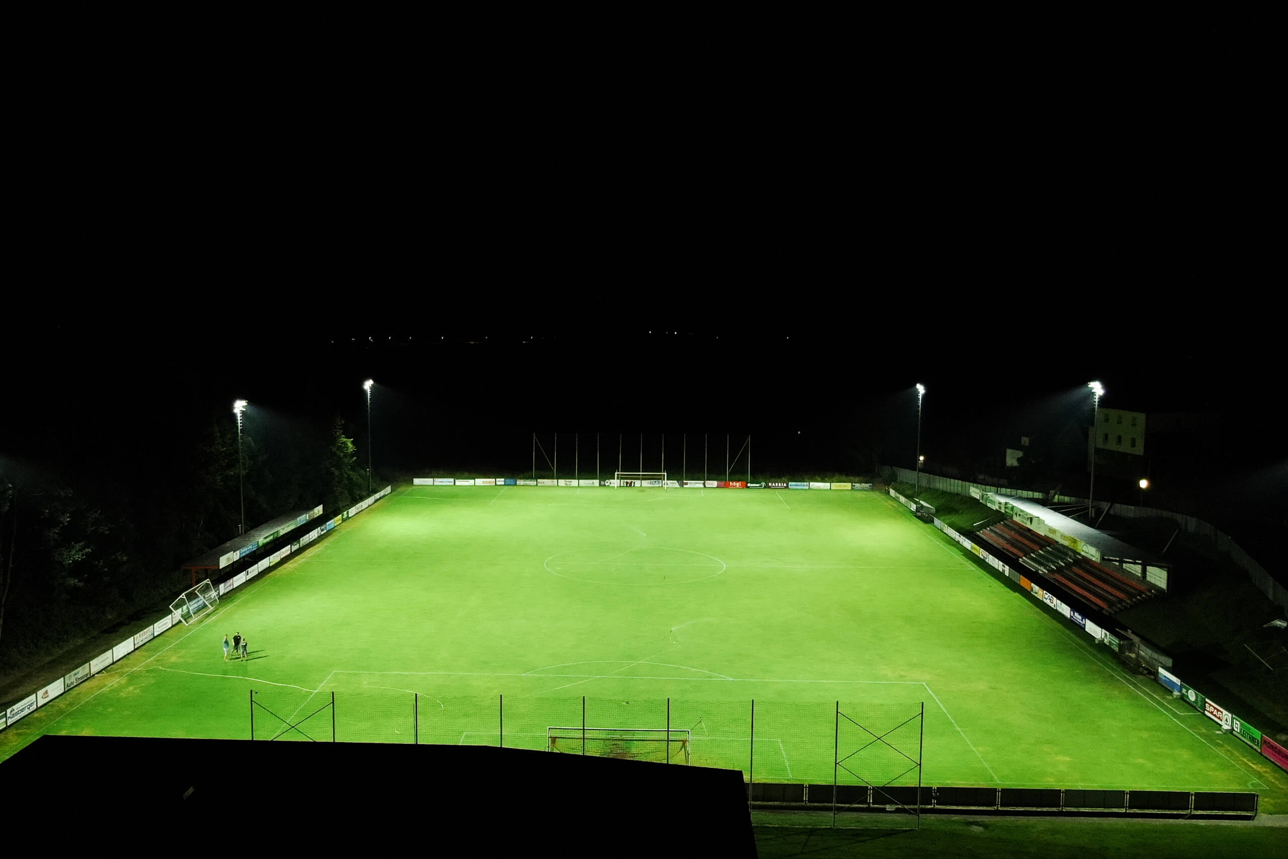 Sportplatzbeleuchtung bei Nacht mit gut beleuchtetem Fußballfeld und Tribüne