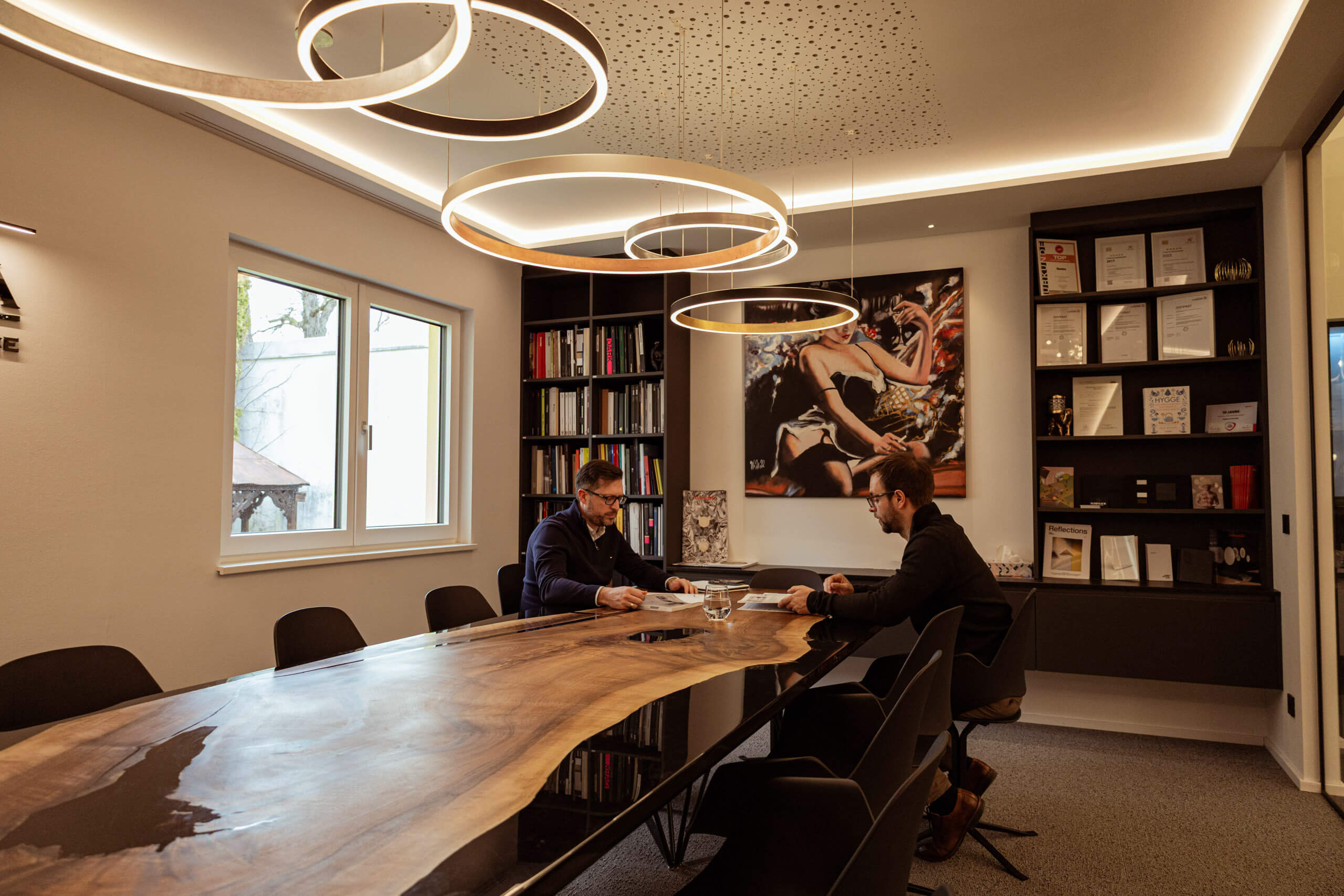 Zwei Männer in einem modernen Büro mit großer Holztafel und indirekter Beleuchtung