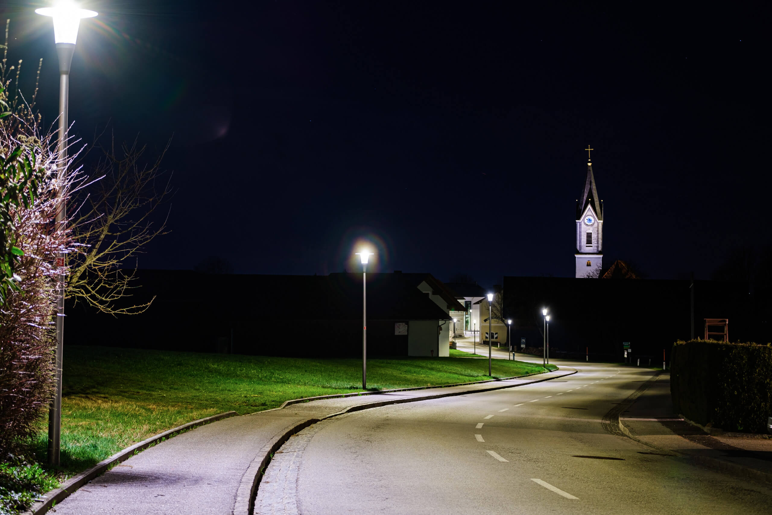 Nachtaufnahme einer beleuchteten Straße mit Kirchturm im Hintergrund – Straßenbeleuchtung von Illumina.