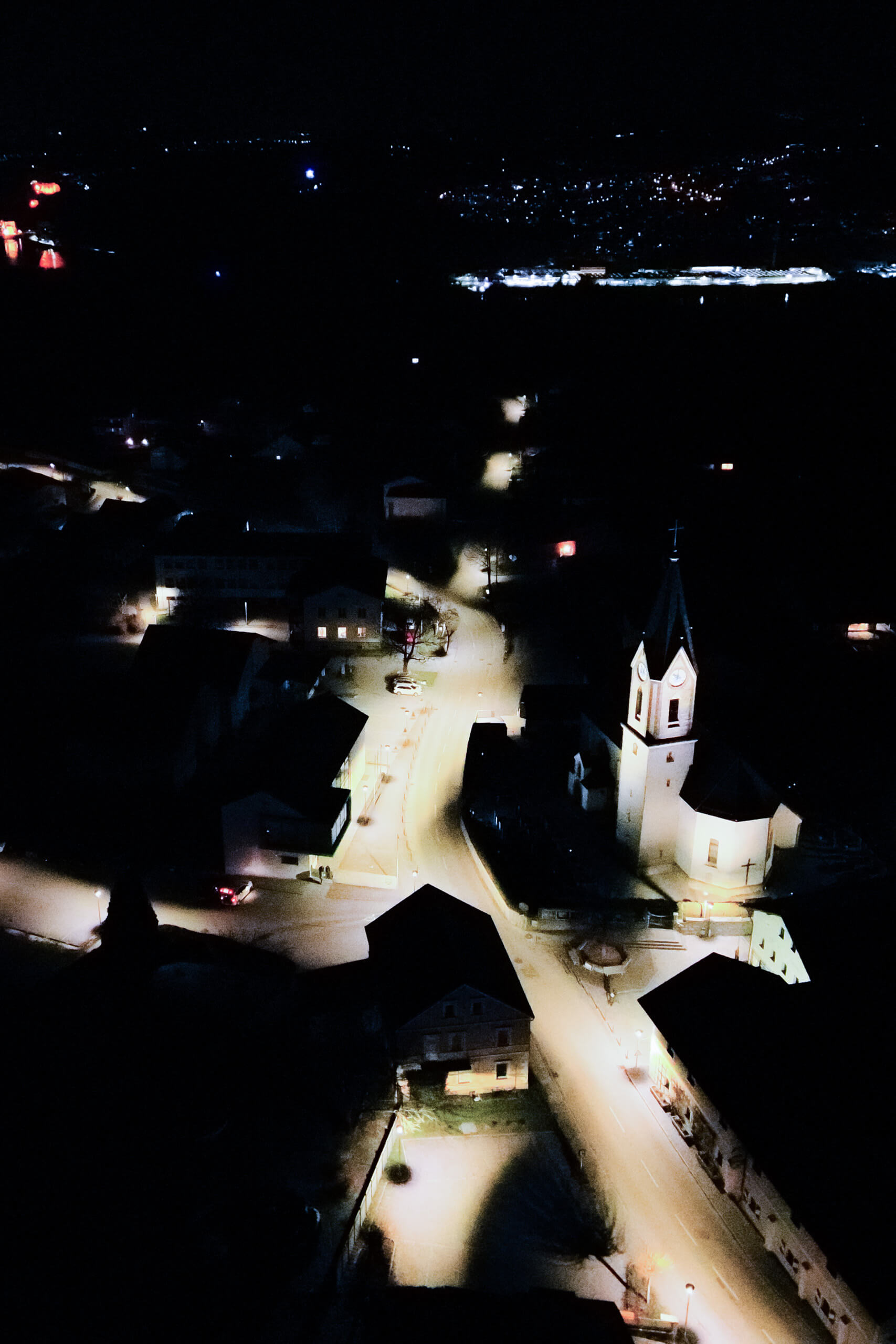 Nachtaufnahme eines Dorfes mit beleuchtetem Kirchturm und Straßen.