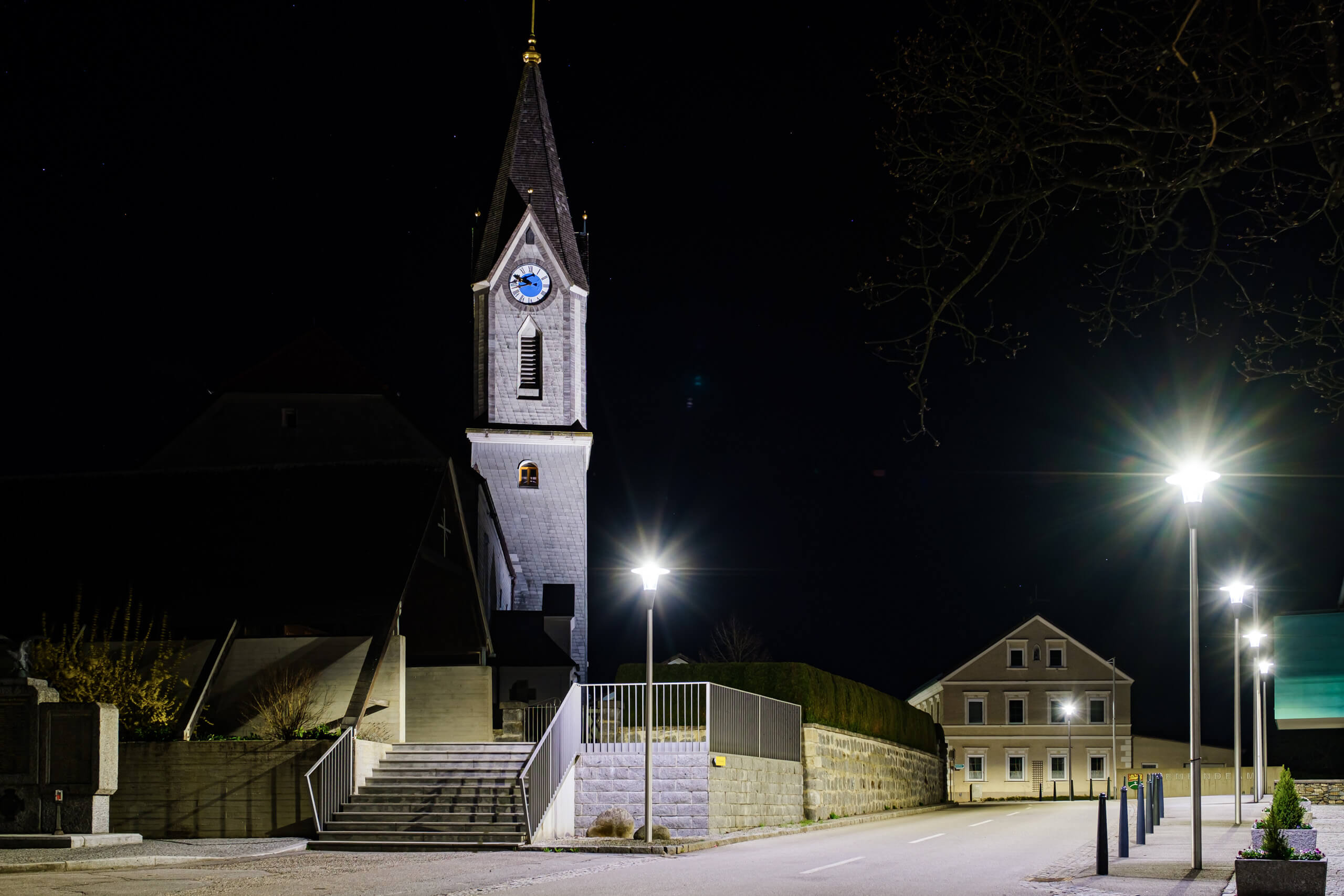 Kirchturm mit Uhr und Straßenbeleuchtung bei Nacht