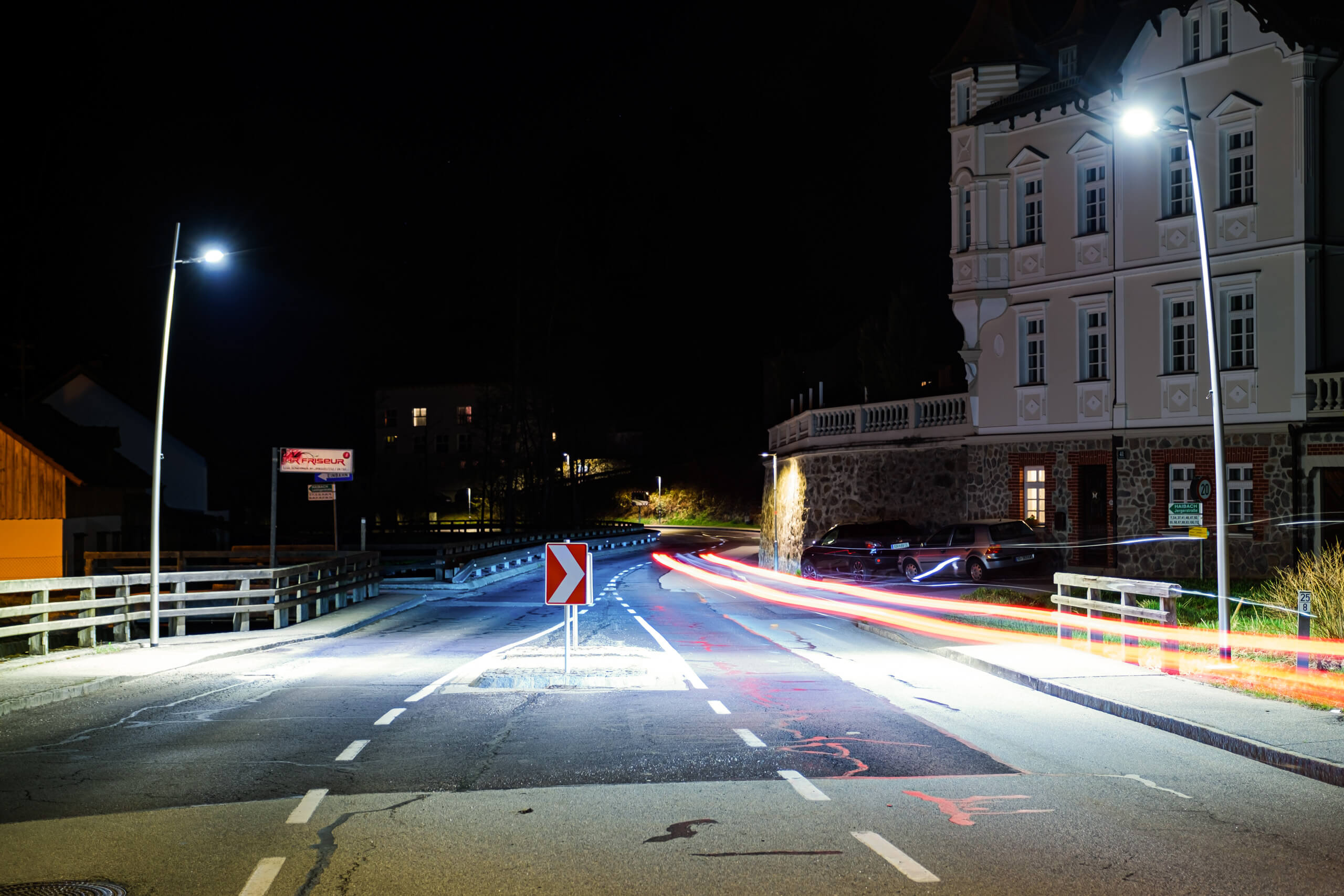 Straßenbeleuchtung mit Lichtspuren von Fahrzeugen vor einem Gebäude bei Nacht