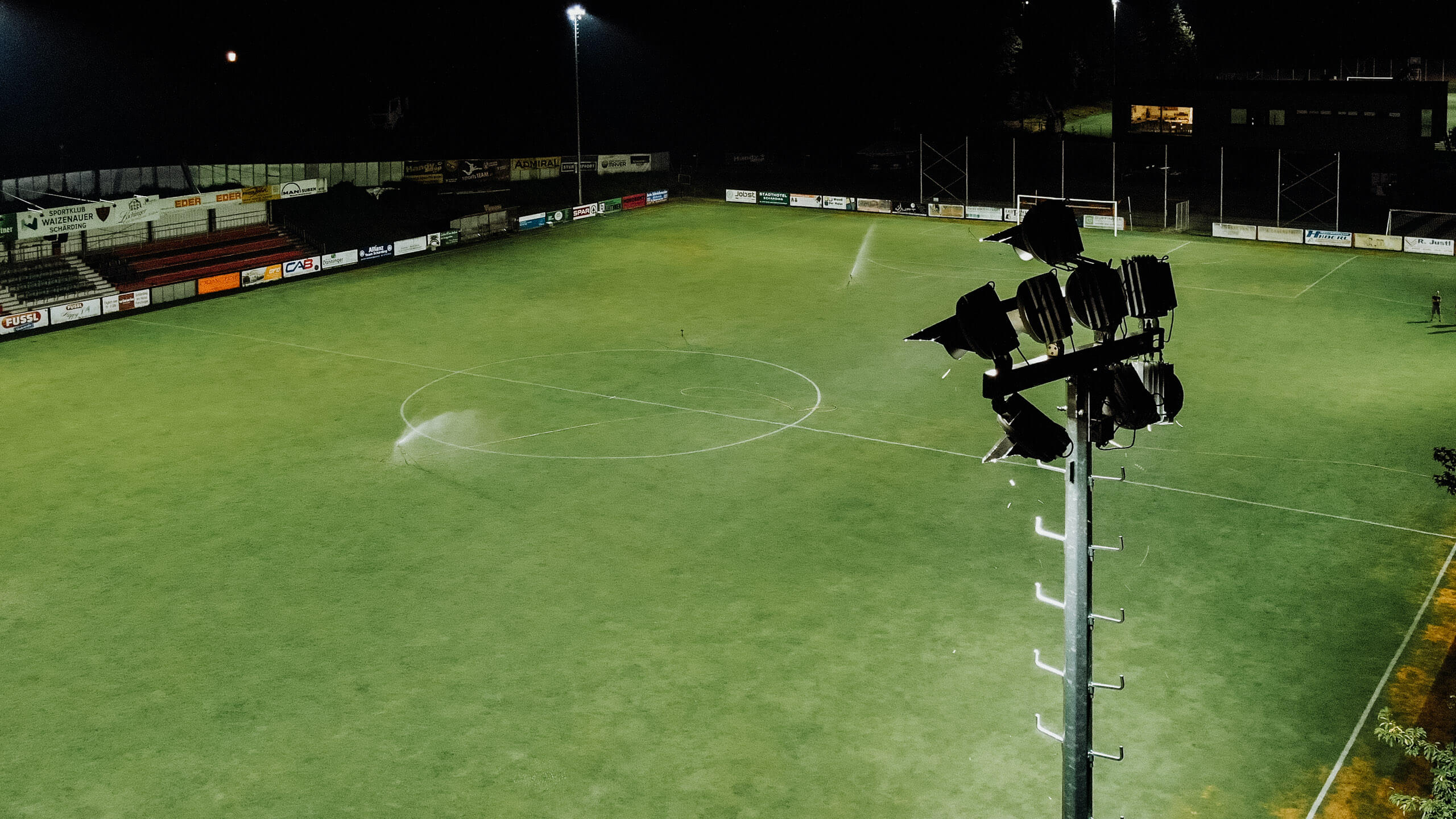 Beleuchteter Fußballplatz mit Flutlichtstrahlern bei Nacht