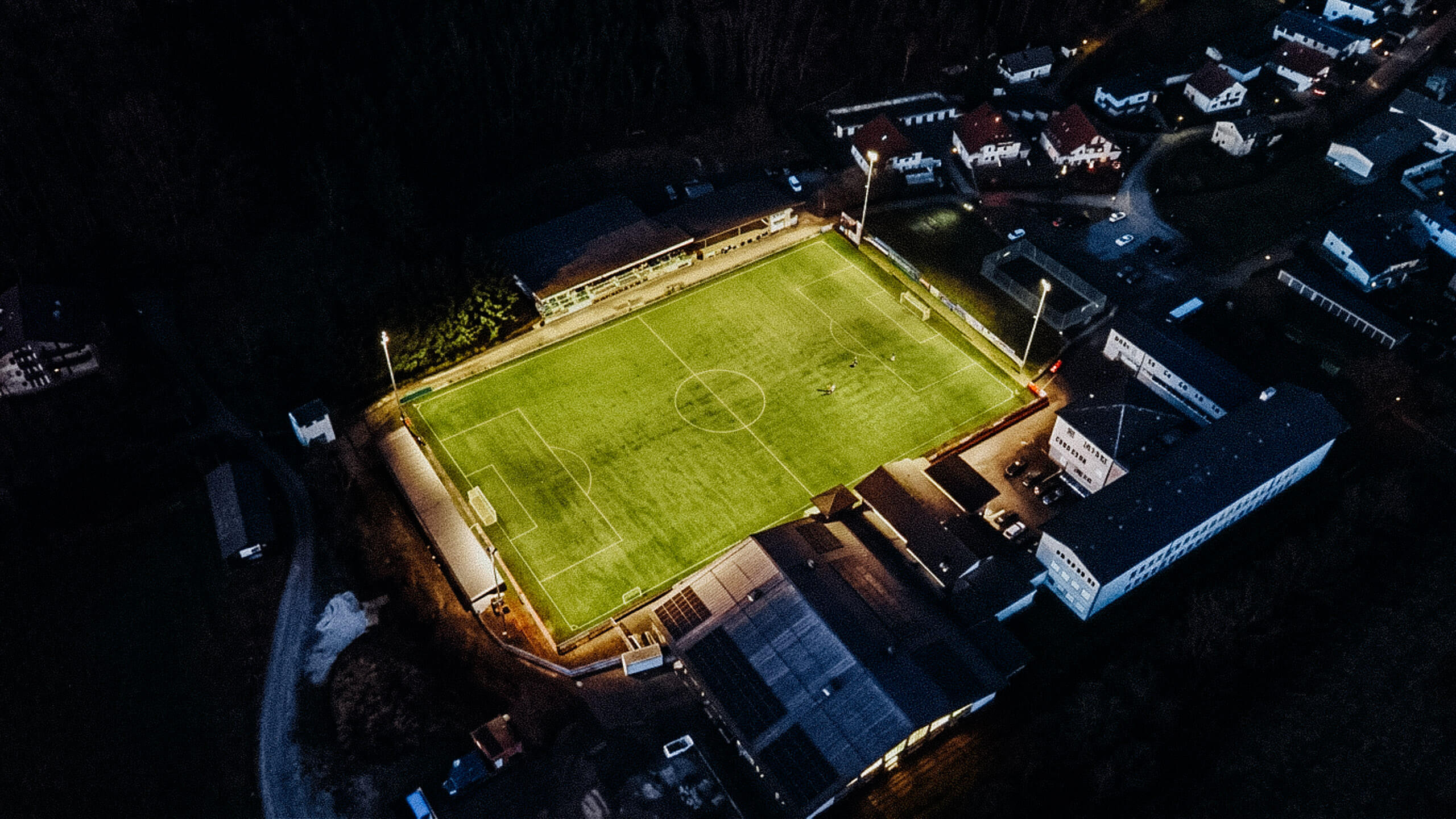 Beleuchteter Fußballplatz bei Nacht mit umliegenden Gebäuden – Sportplatzbeleuchtung von Illumina.