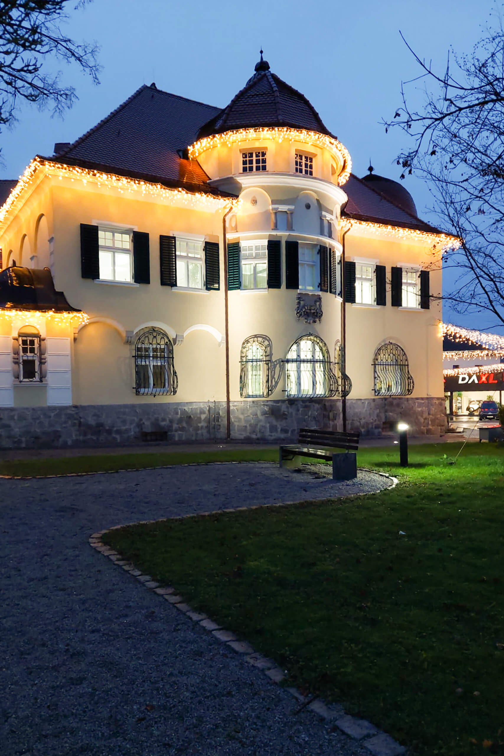 Beleuchtetes Gebäude mit Weihnachtsbeleuchtung und Parkbank im Abendlicht