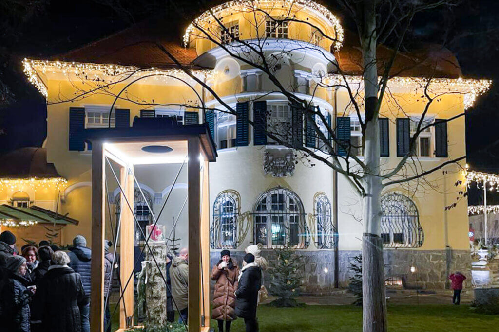 Festlich beleuchtetes Gebäude mit Menschenmenge und Weihnachtsdeko