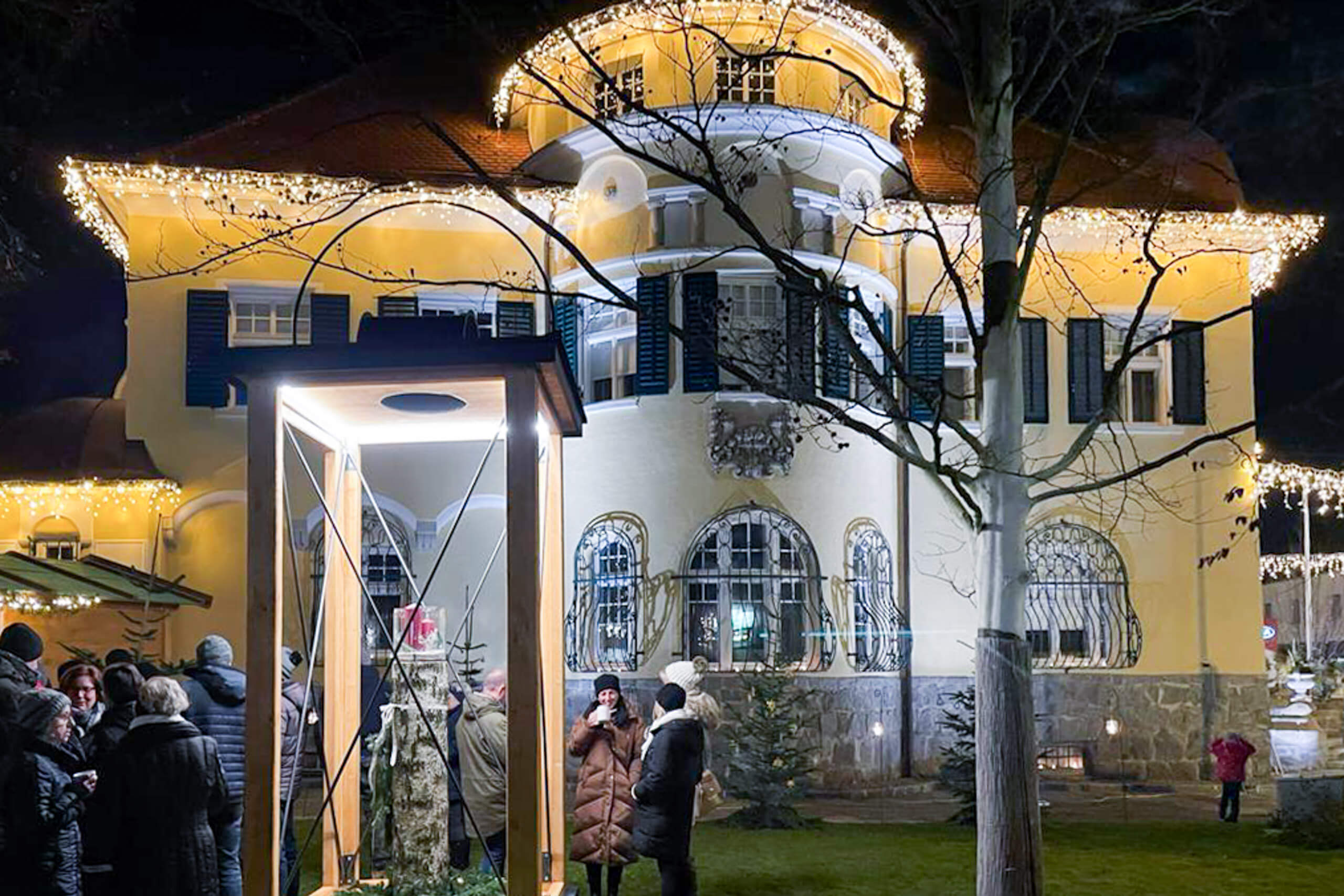Festlich beleuchtetes Gebäude mit Menschenmenge und Weihnachtsdeko