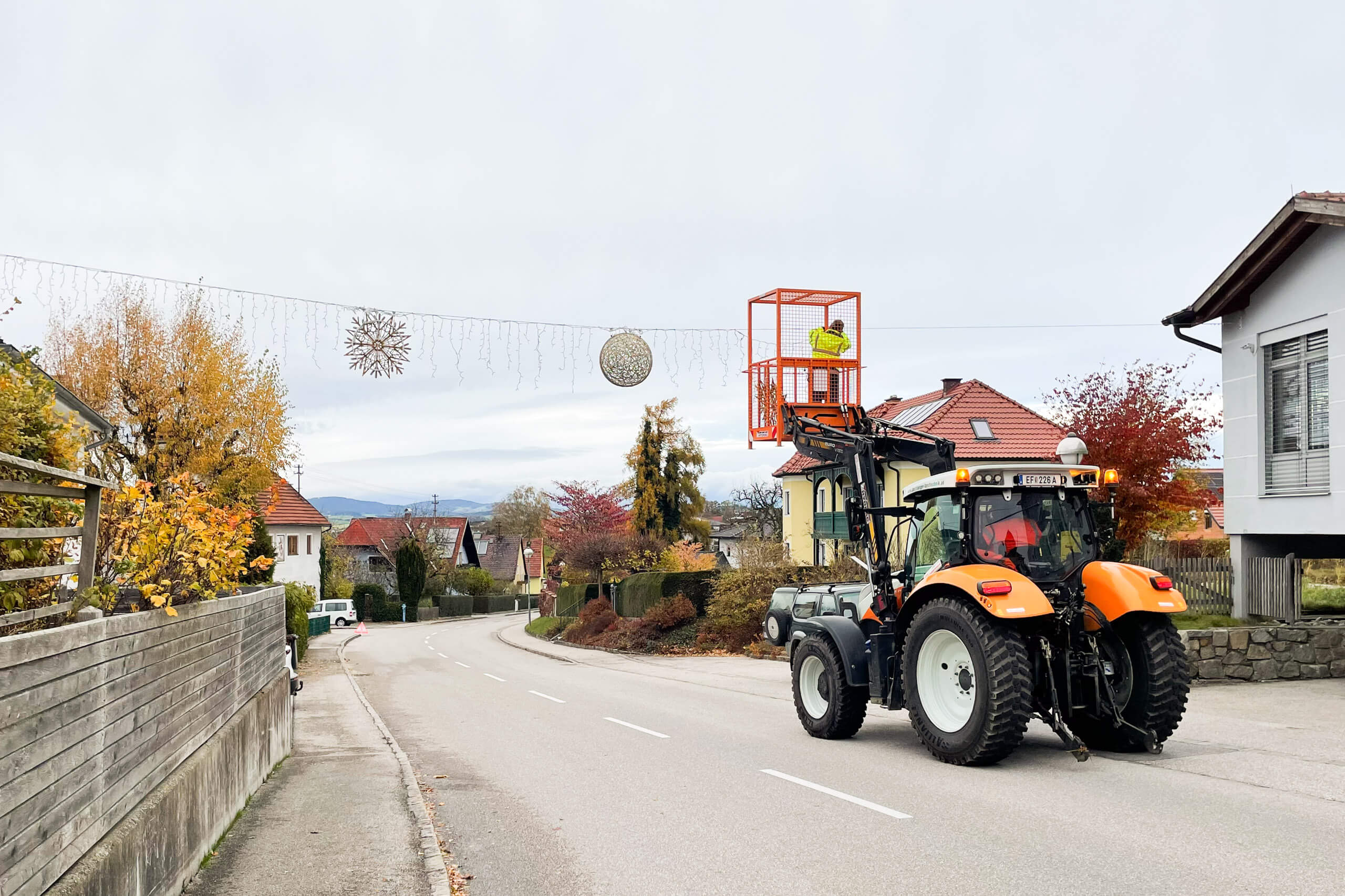 Traktor mit Arbeitskorb installiert Weihnachtsbeleuchtung in Wohngebiet.
