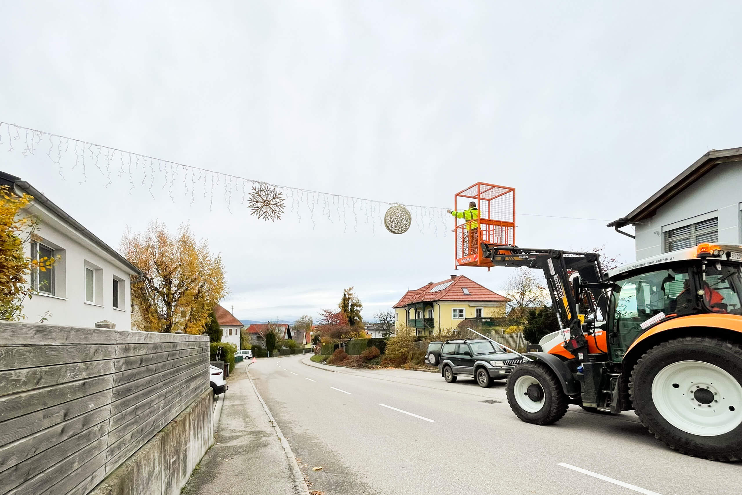 Straßenbeleuchtung: Mann im Hubsteiger montiert Lichterkette über Straße.