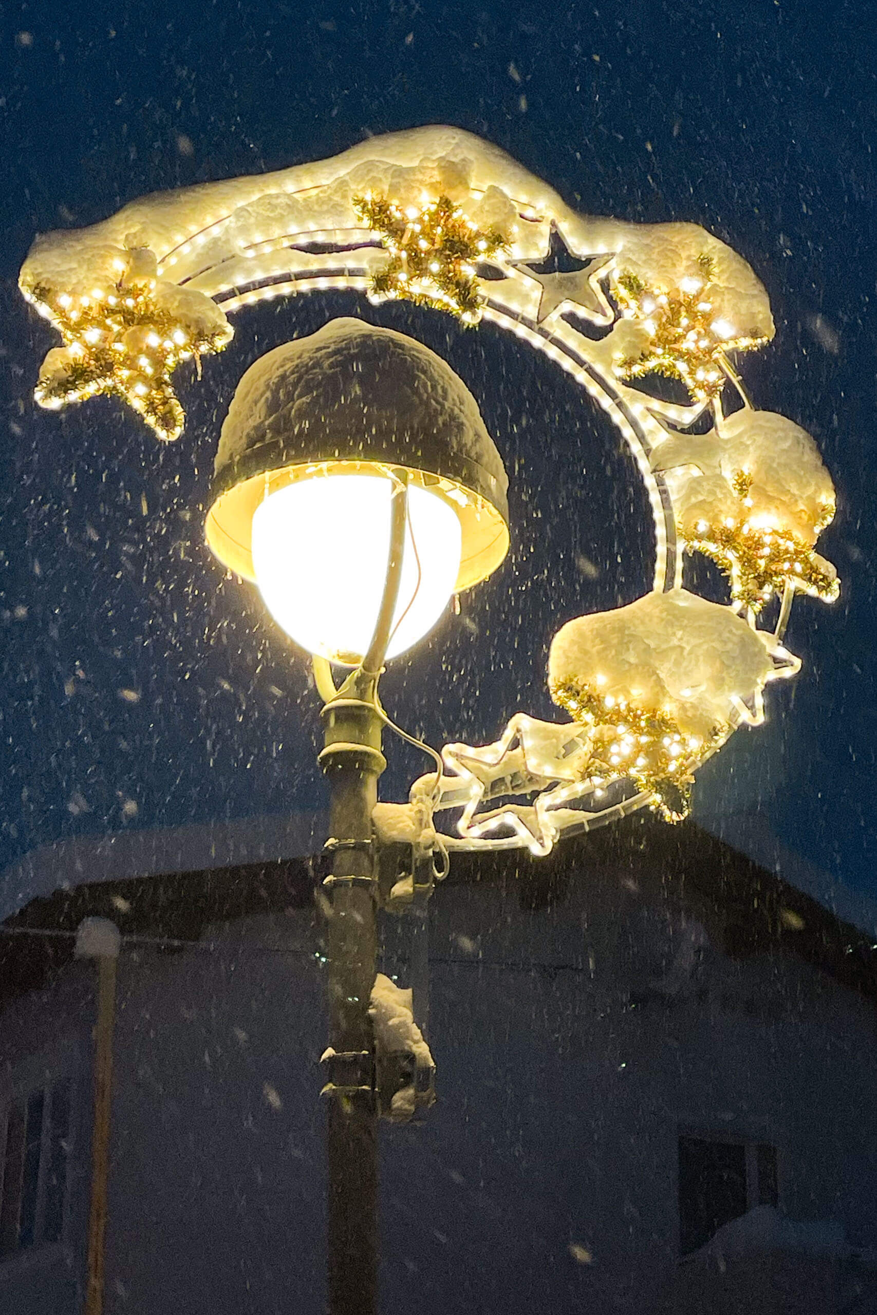 Straßenlaterne mit Weihnachtsbeleuchtung und Sternen im Schneefall