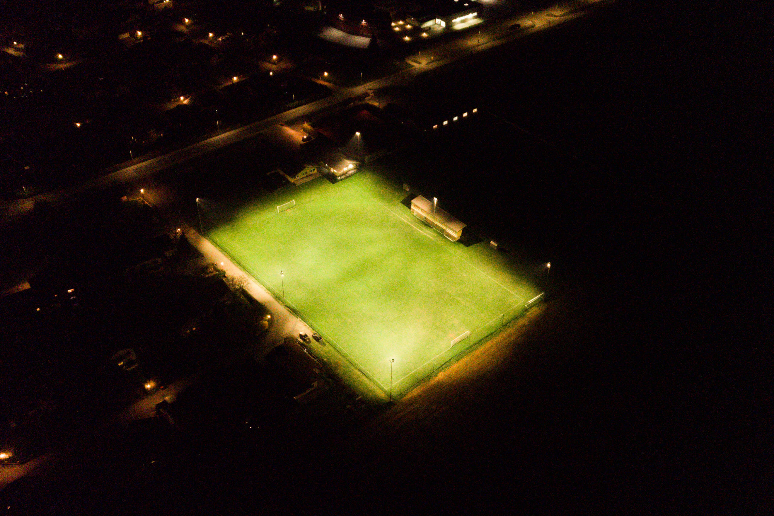 Sportplatzbeleuchtung mit leuchtenden Feldern und Tribünen bei Nacht