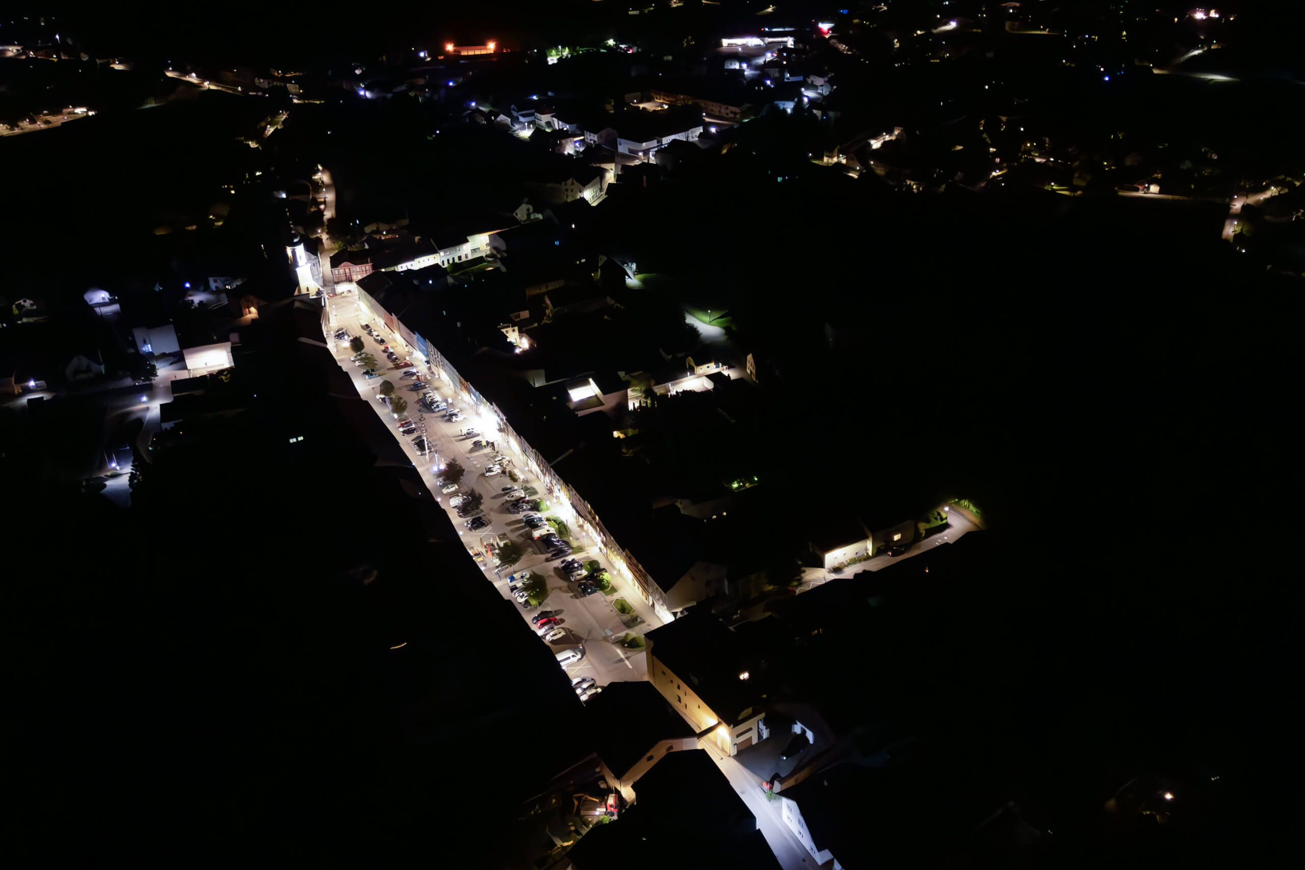 Nachtaufnahme einer beleuchteten Straße mit Parkplätzen und Gebäuden, Lichtplanung von Illumina.