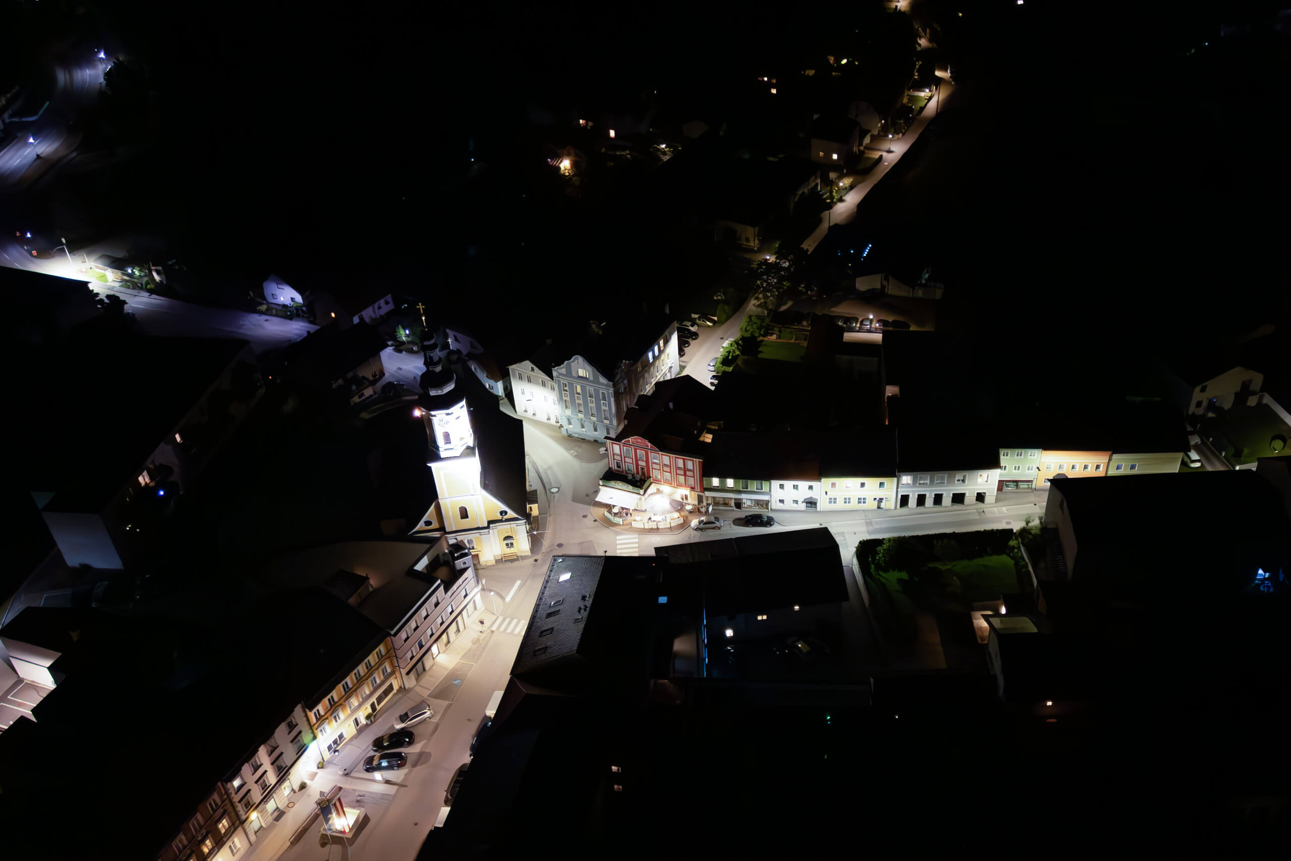 Nachtansicht einer beleuchteten Stadt mit Kirchturm und Straßenbeleuchtung