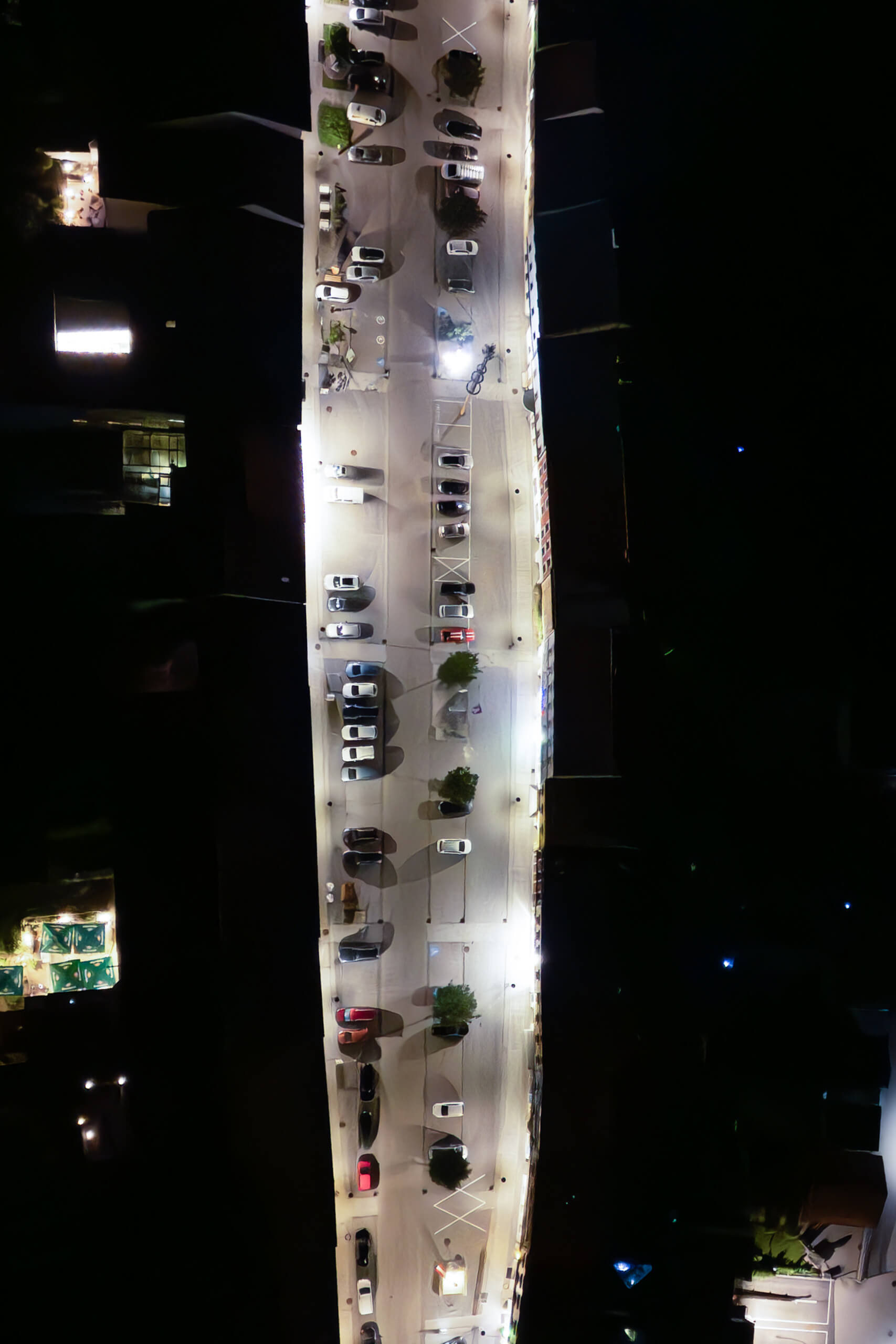Luftaufnahme einer beleuchteten Straße mit parkenden Autos bei Nacht
