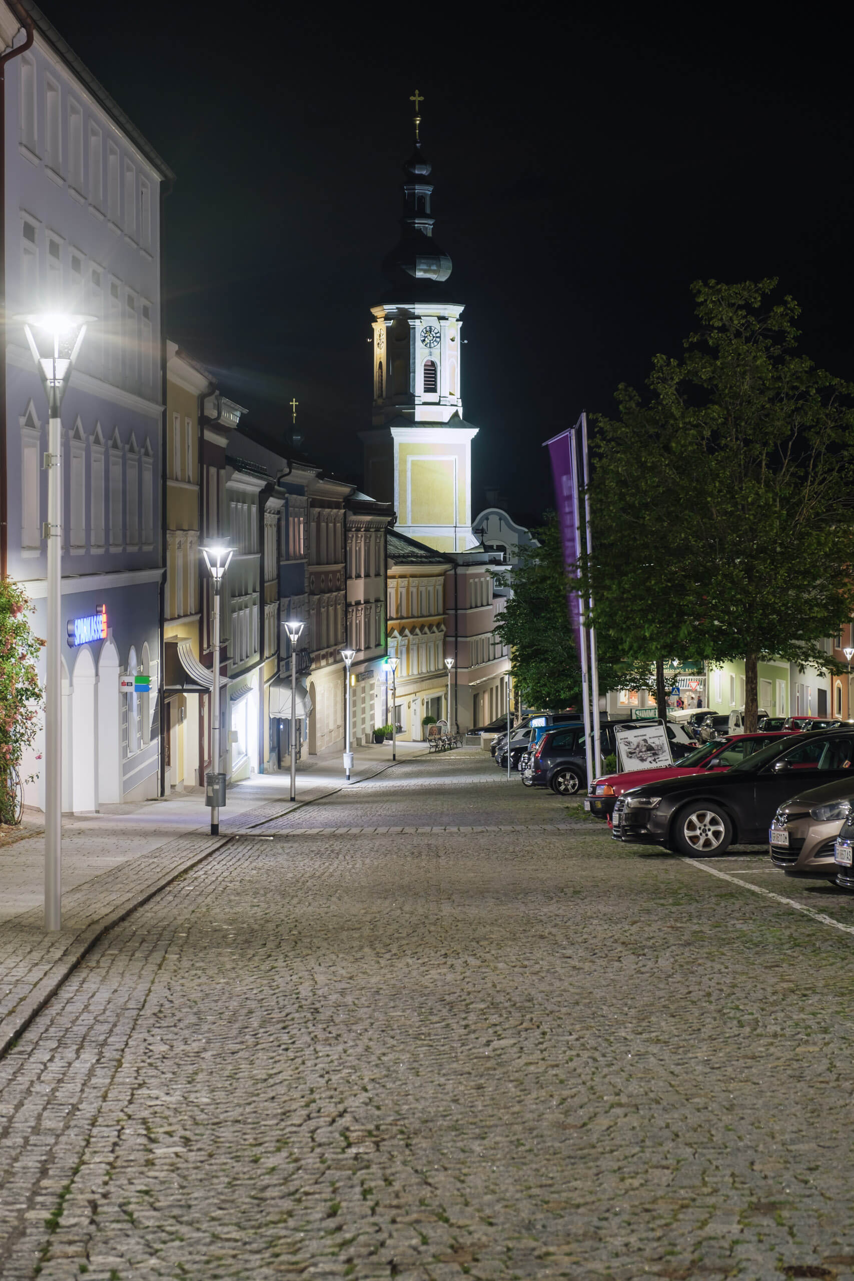 Beleuchtete Gasse mit Kopfsteinpflaster und Kirchturm in Österreich, Straßenbeleuchtung von Illumina