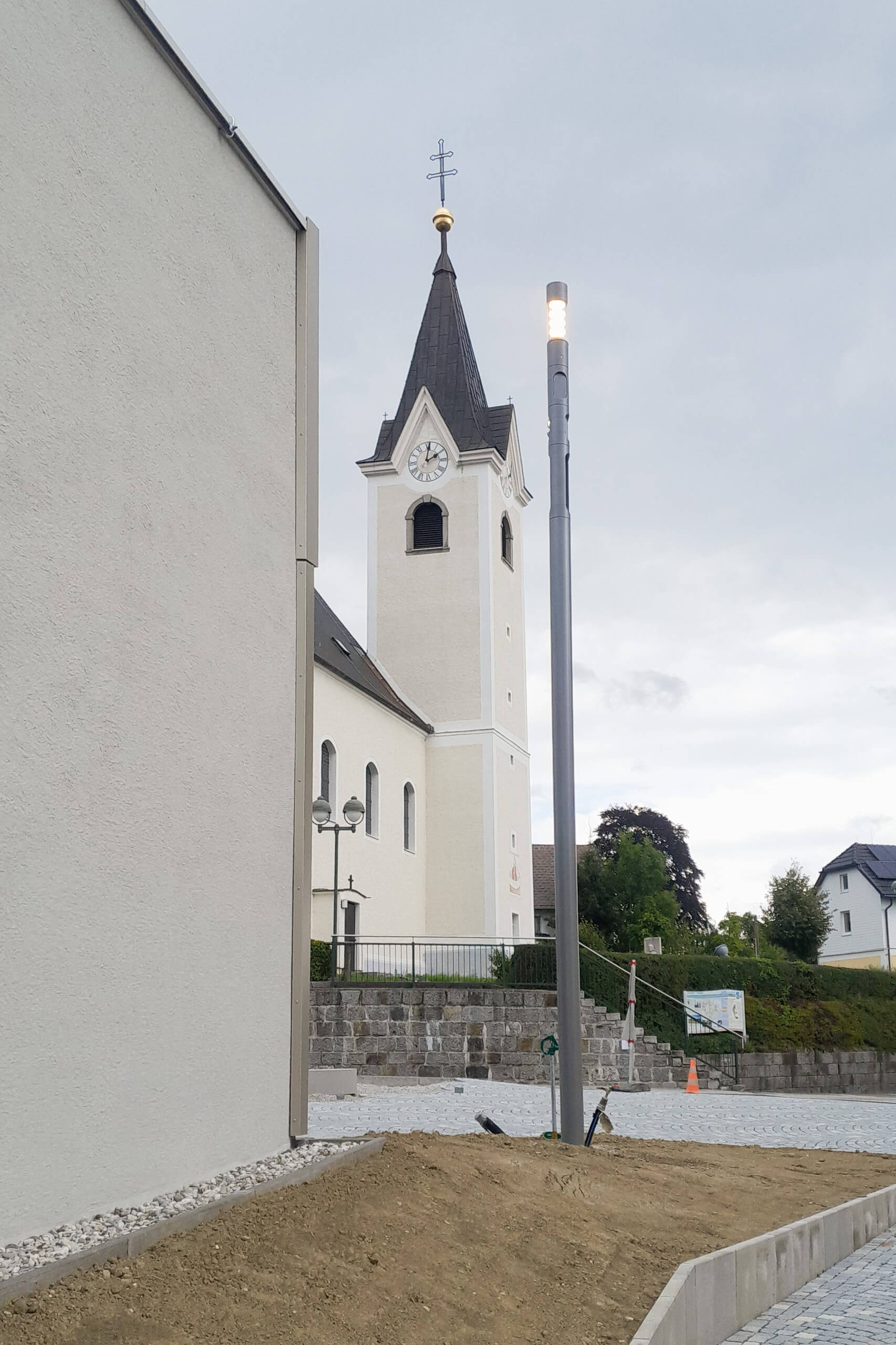 Kirchturm mit Uhr und moderner Straßenlaterne vor bewölktem Himmel