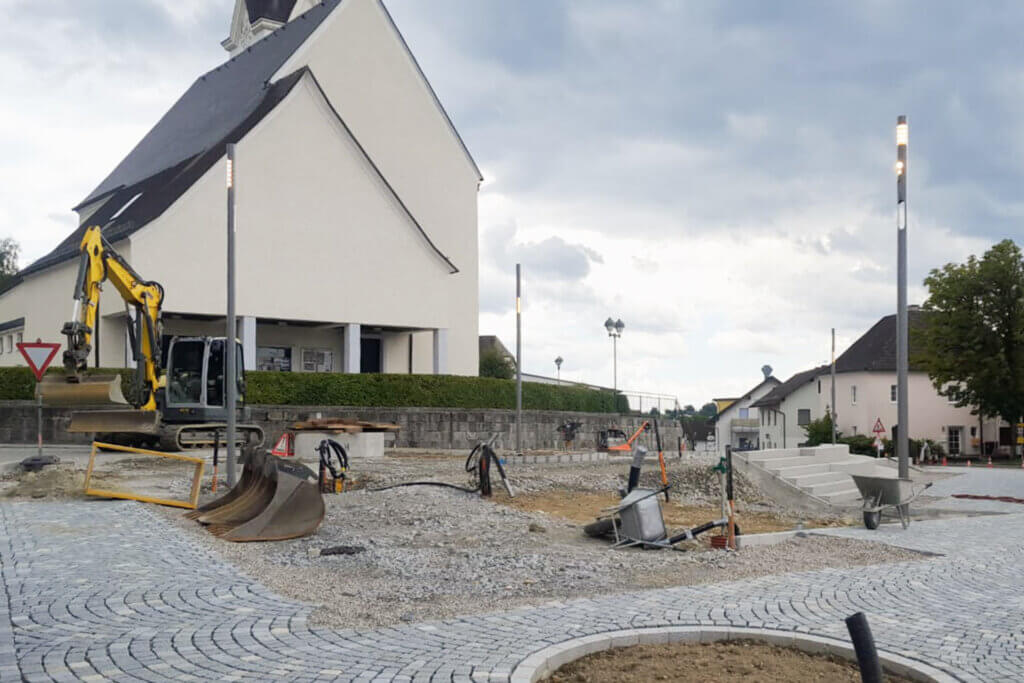 Baustelle mit Bagger und neuem Pflaster vor einem Gebäude, moderne Straßenbeleuchtung