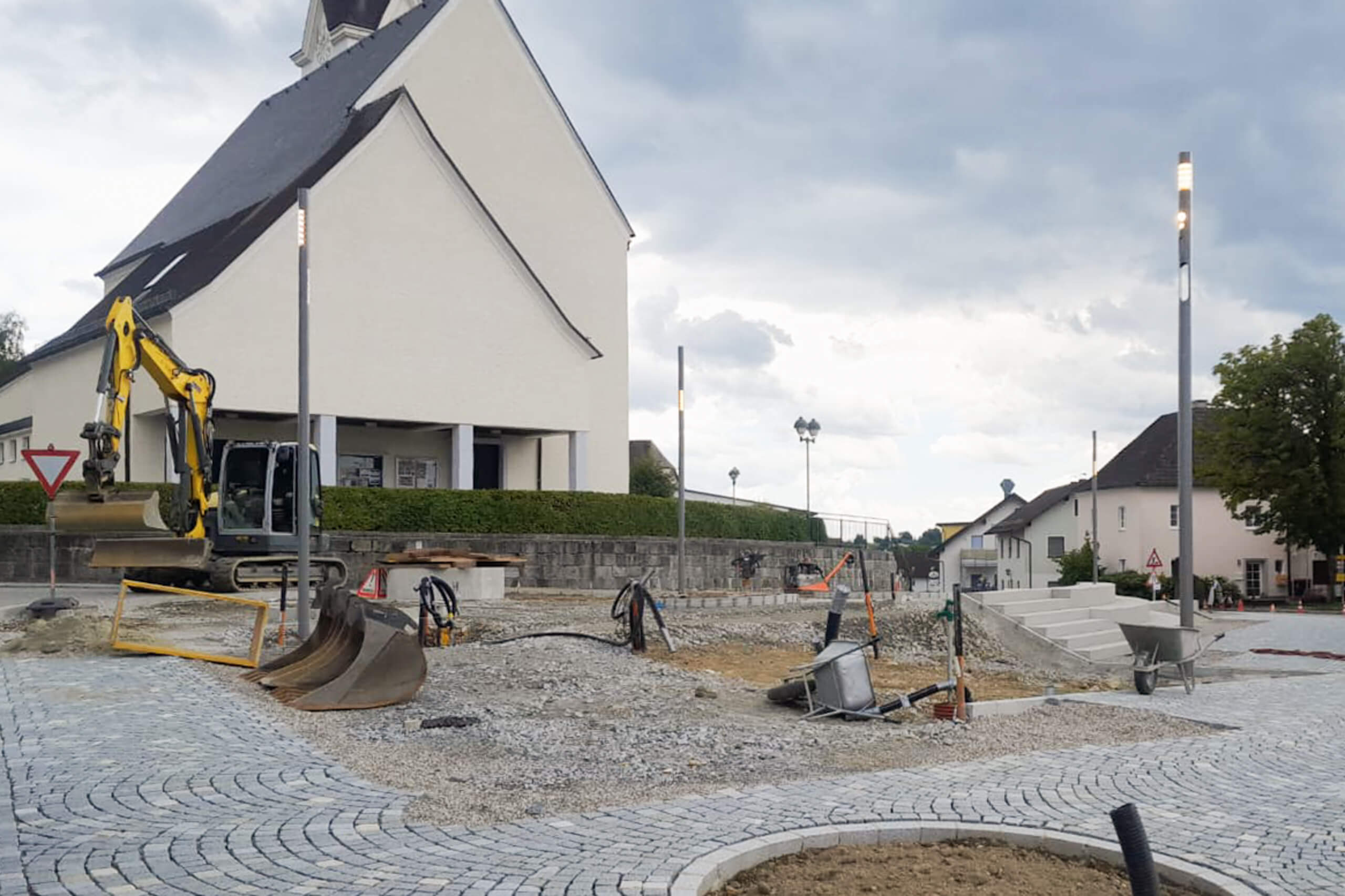 Baustelle mit Bagger und neuem Pflaster vor einem Gebäude, moderne Straßenbeleuchtung