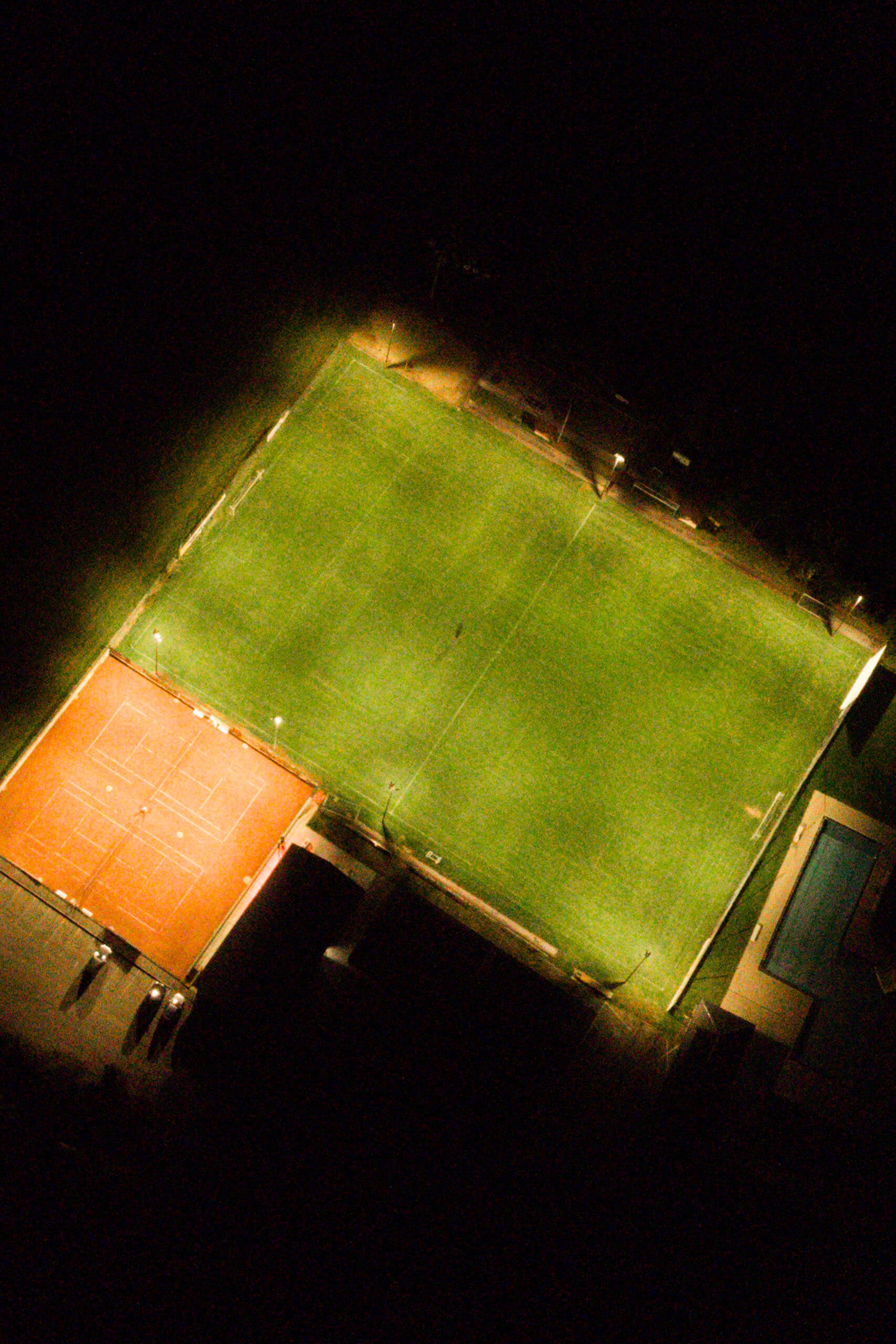 Beleuchtetes Sportfeld mit Fußballplatz und Tennisplatz bei Nacht