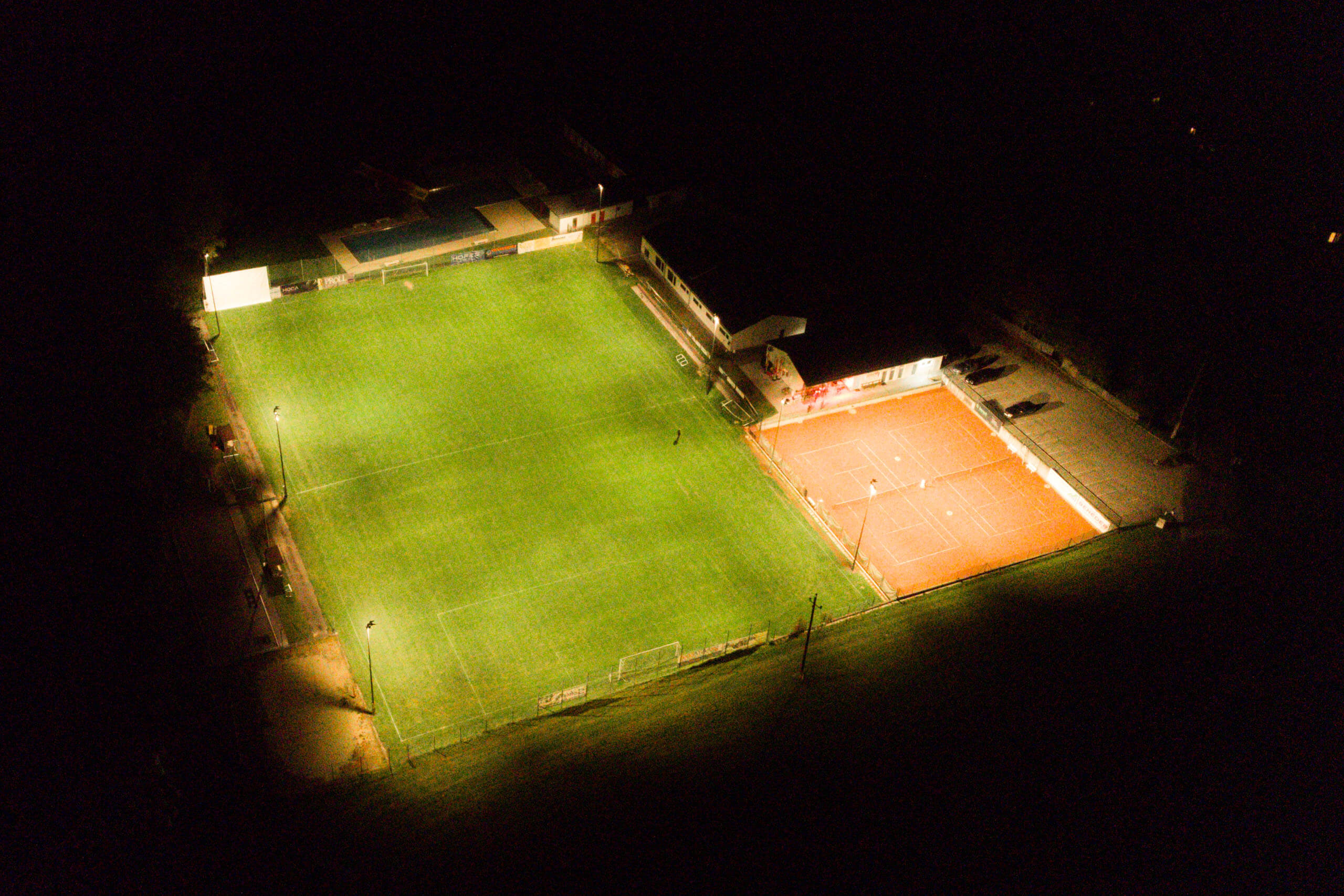 Sportplatzbeleuchtung von Illumina bei Nacht mit beleuchtetem Fußballfeld und Tennisplatz