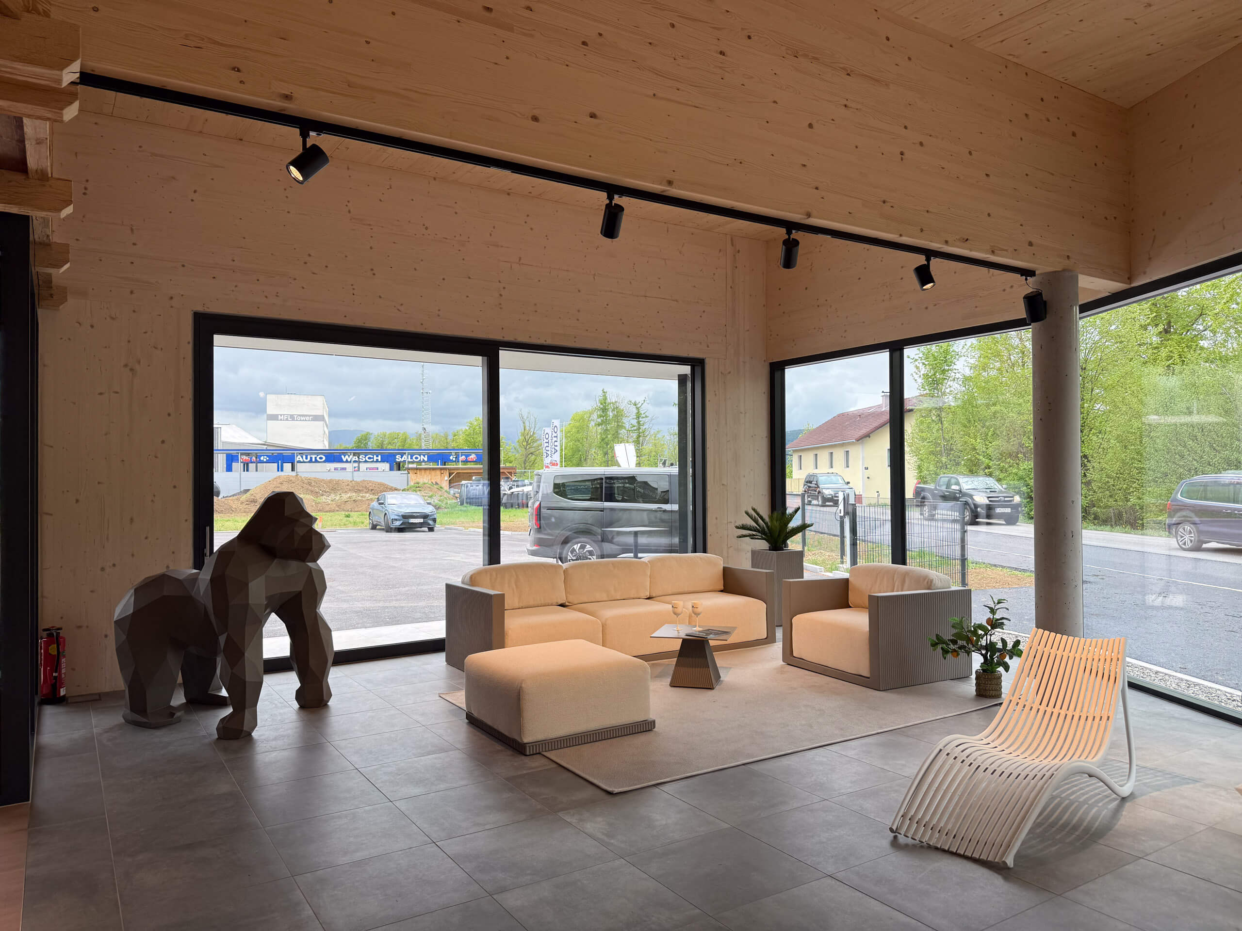Moderne Architekturbeleuchtung: Helle Holzdecke, Glasfront, Loungemöbel und Gorilla-Skulptur.
