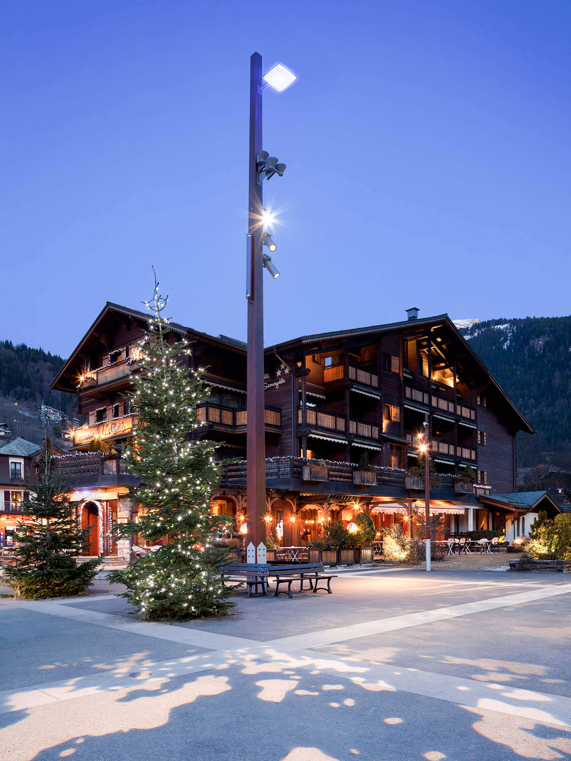 Beleuchtetes Holzgebäude mit Weihnachtsbaum und Stadtmobiliar bei Nacht