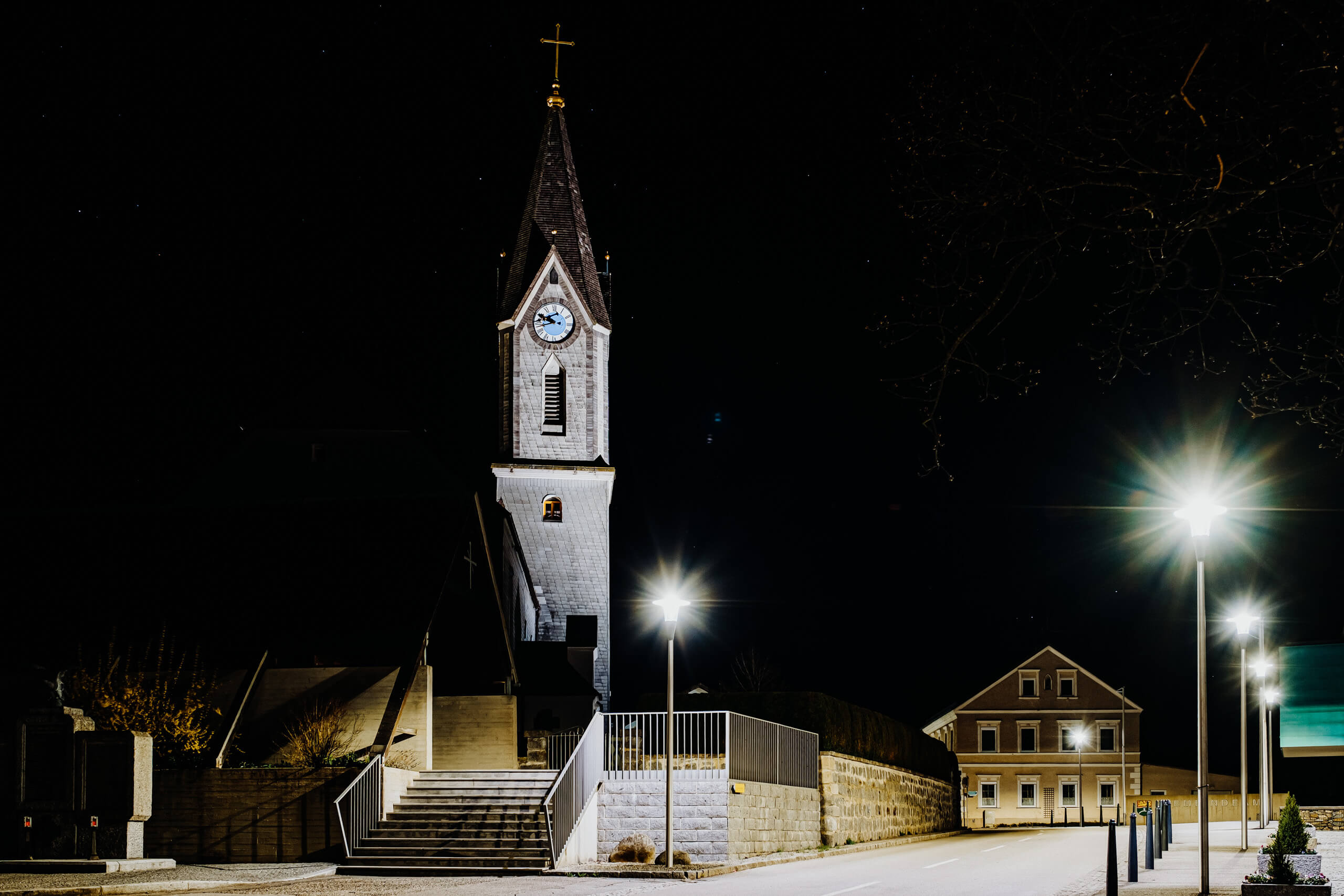 Architekturbeleuchtung: Kirchturm und Haus mit heller Anstrahlung im Dunkeln
