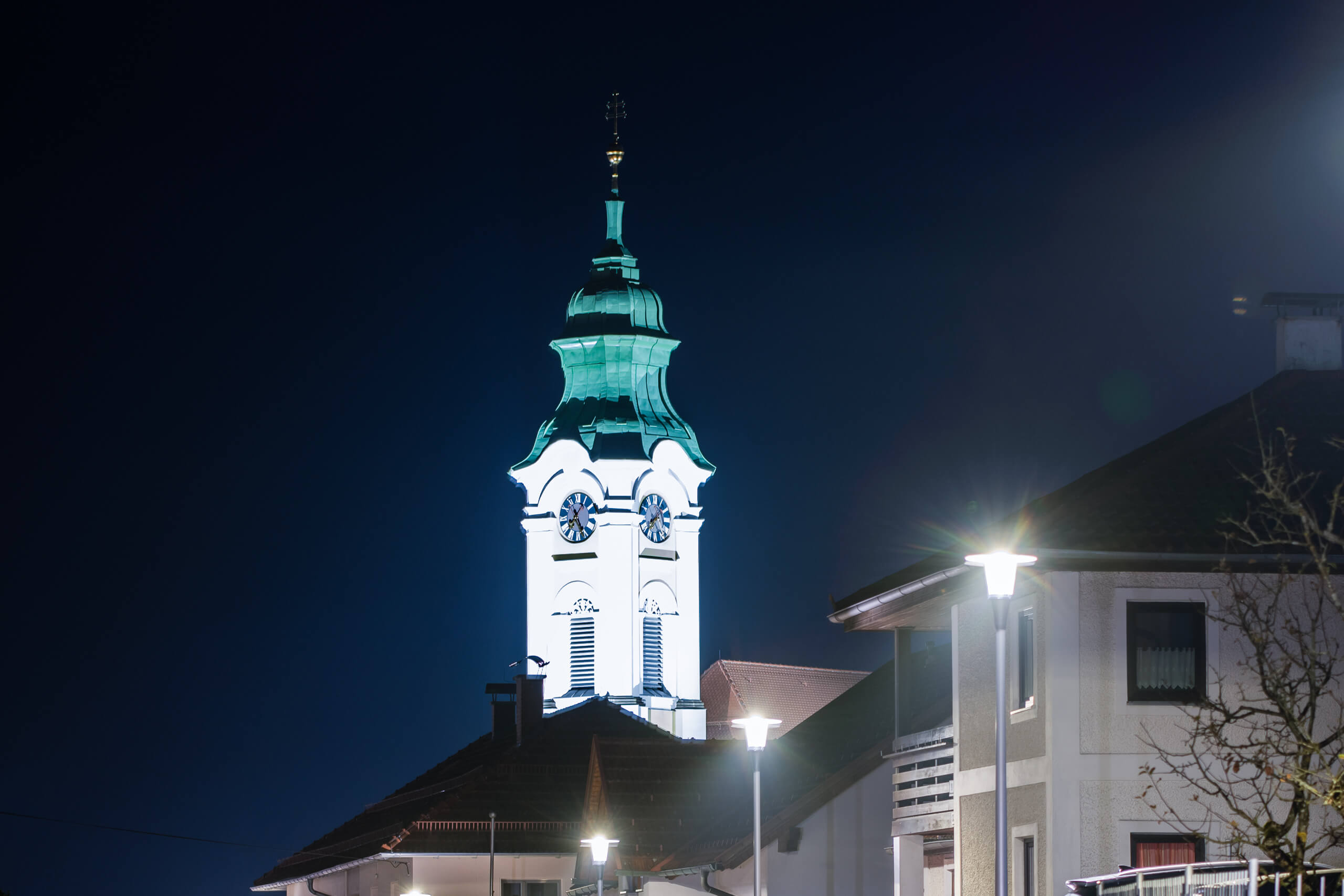 Kirchturm mit grüner Kuppel und Uhr bei Nacht, beleuchtet von Straßenlaternen