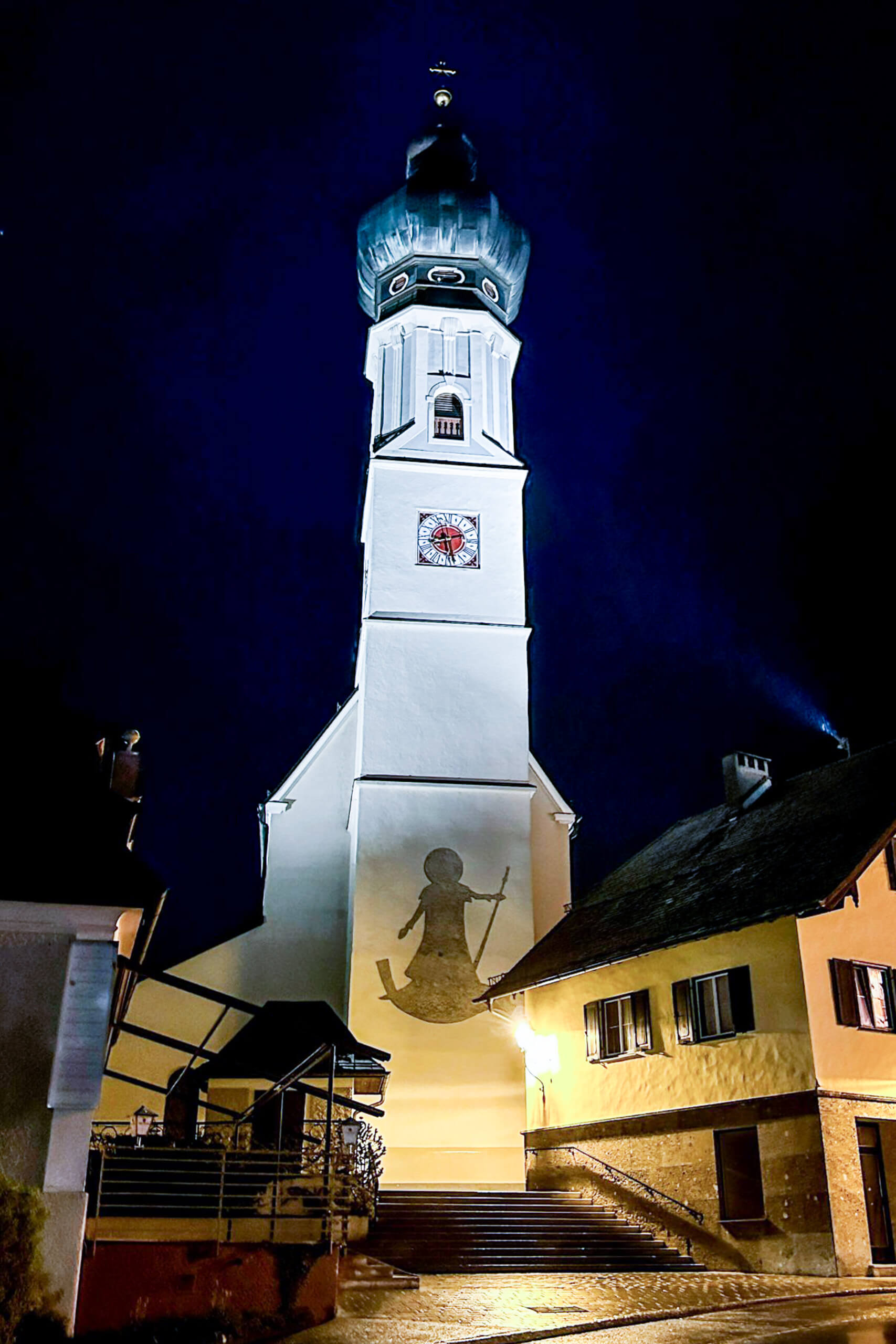 Kirchturm mit Glockenspiel und Wandmalerei bei Nacht