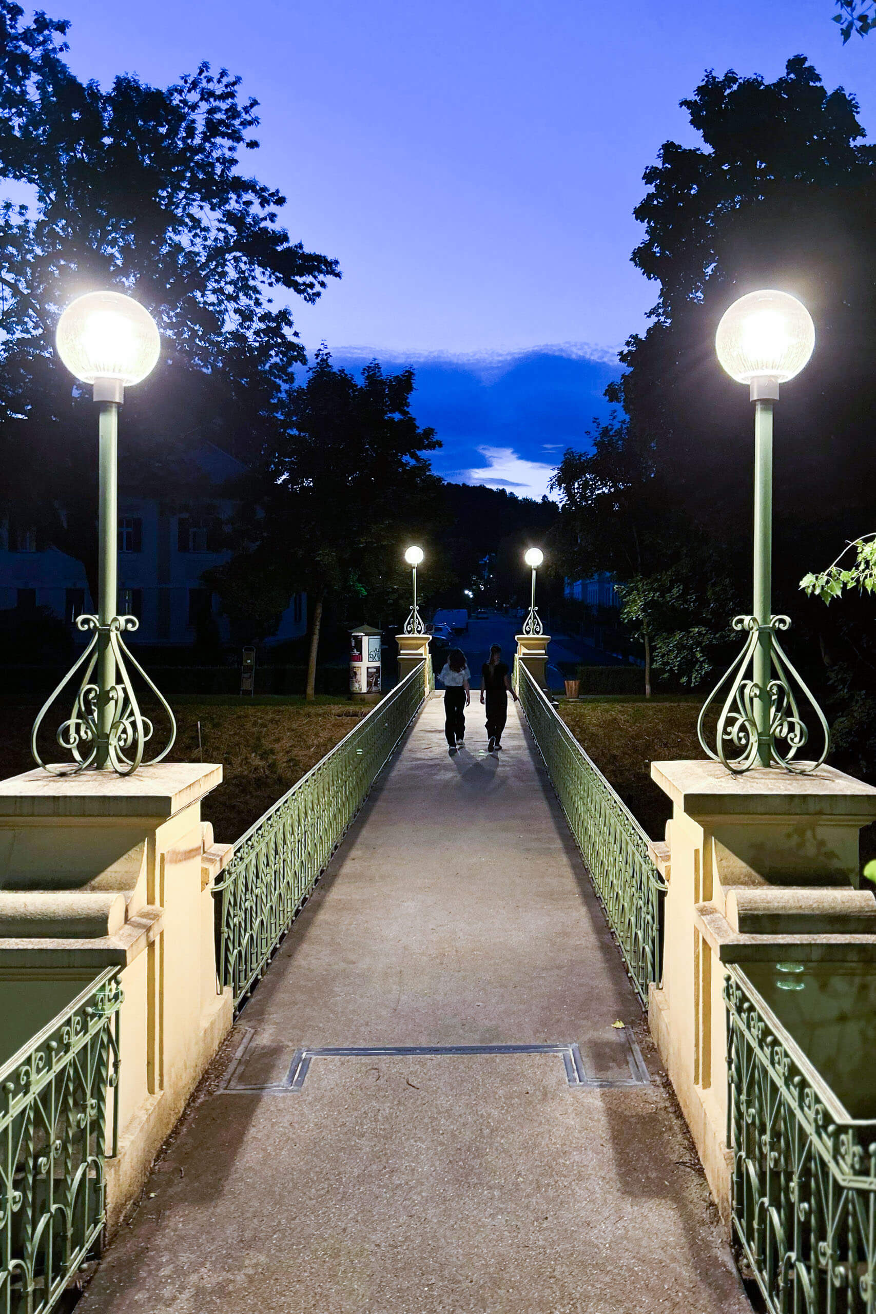 Zwei Personen gehen abends über eine beleuchtete Brücke mit Laternen. Lichtplanung von Illumina.