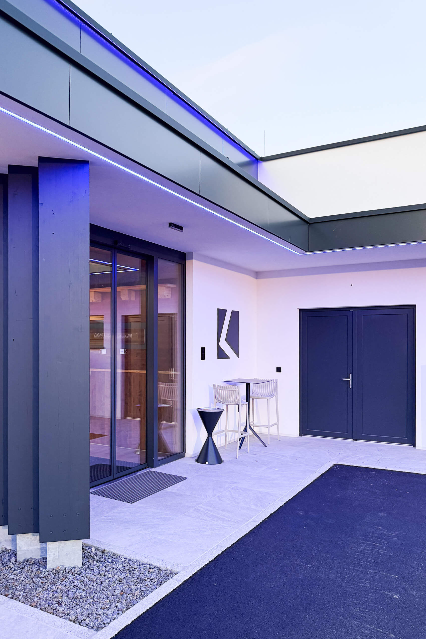 Moderne Fassade mit blau beleuchtetem Eingangsbereich und Außenbestuhlung