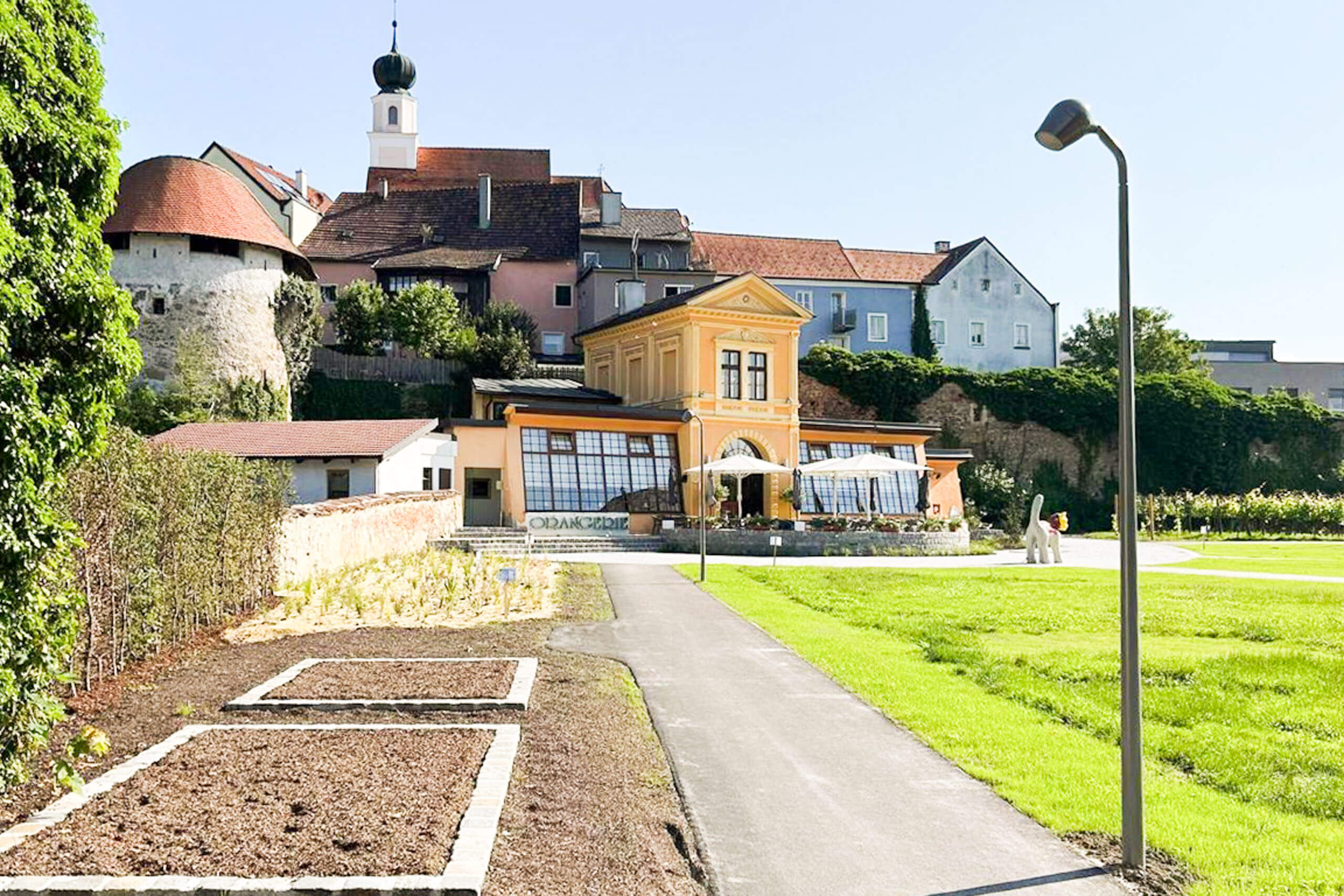 Außenansicht eines modernen Restaurants mit großen Fenstern und Blick auf eine Grünanlage, beleuchtet von natürlichem Tageslicht.
