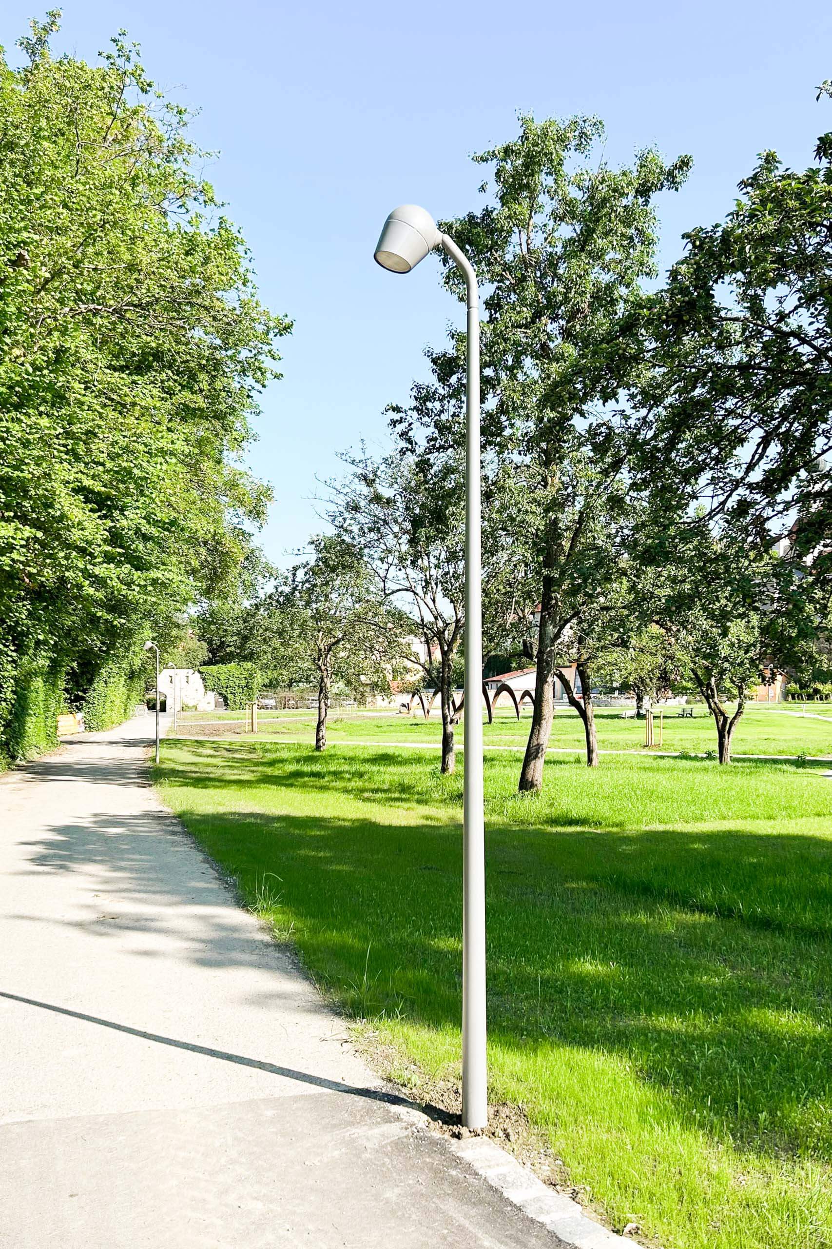 Straßenlaterne im sonnigen Park mit Gehweg und Bäumen