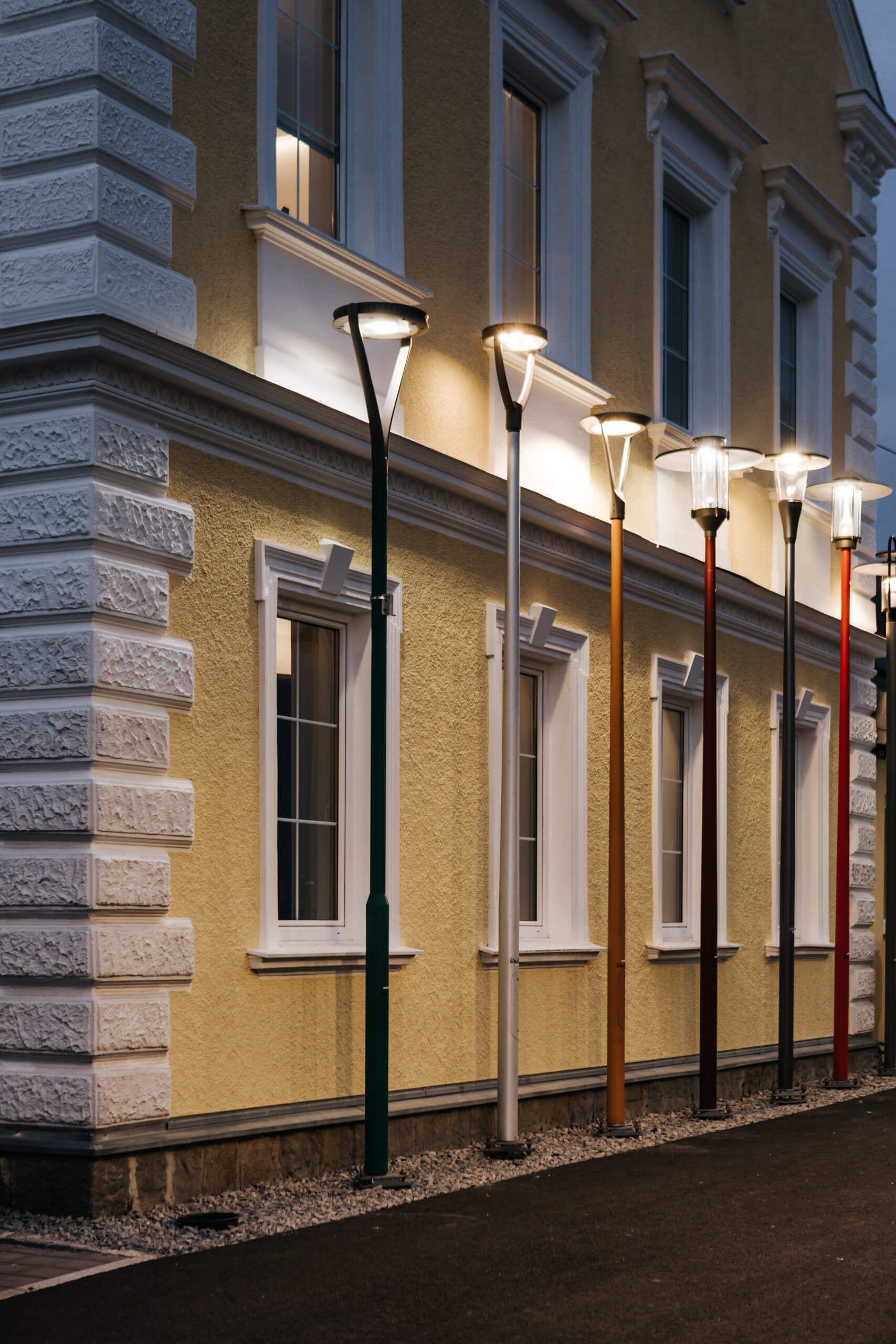 Illuminas Außenbeleuchtung: Mehrere moderne Stehleuchten beleuchten eine gelbe Hausfassade bei Dämmerung.