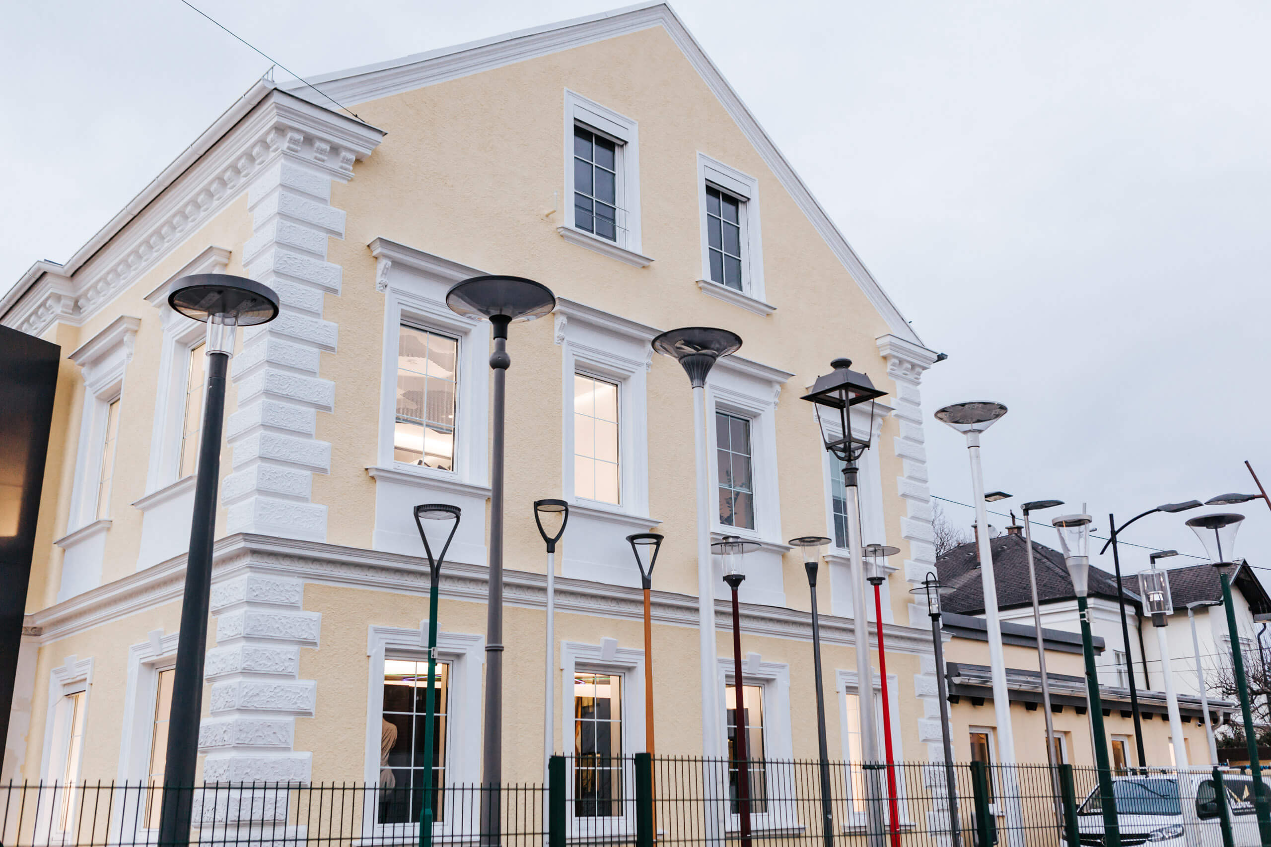 Moderne Straßenlaternen und Architekturbeleuchtung vor einem gelben Gebäude.