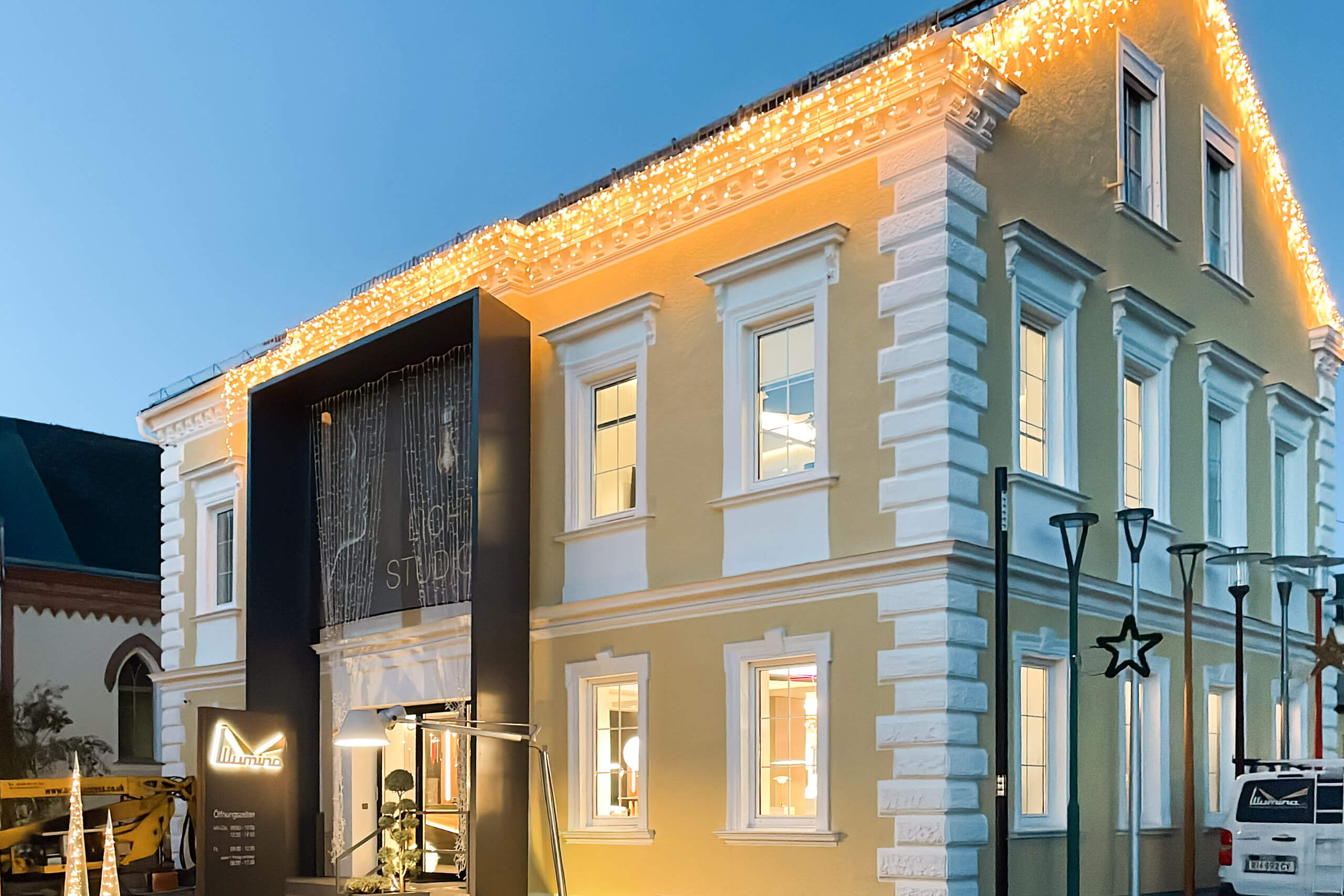 Illumina Lichtplanung: Gelbes Gebäude mit Weihnachtsbeleuchtung und moderner Fassade