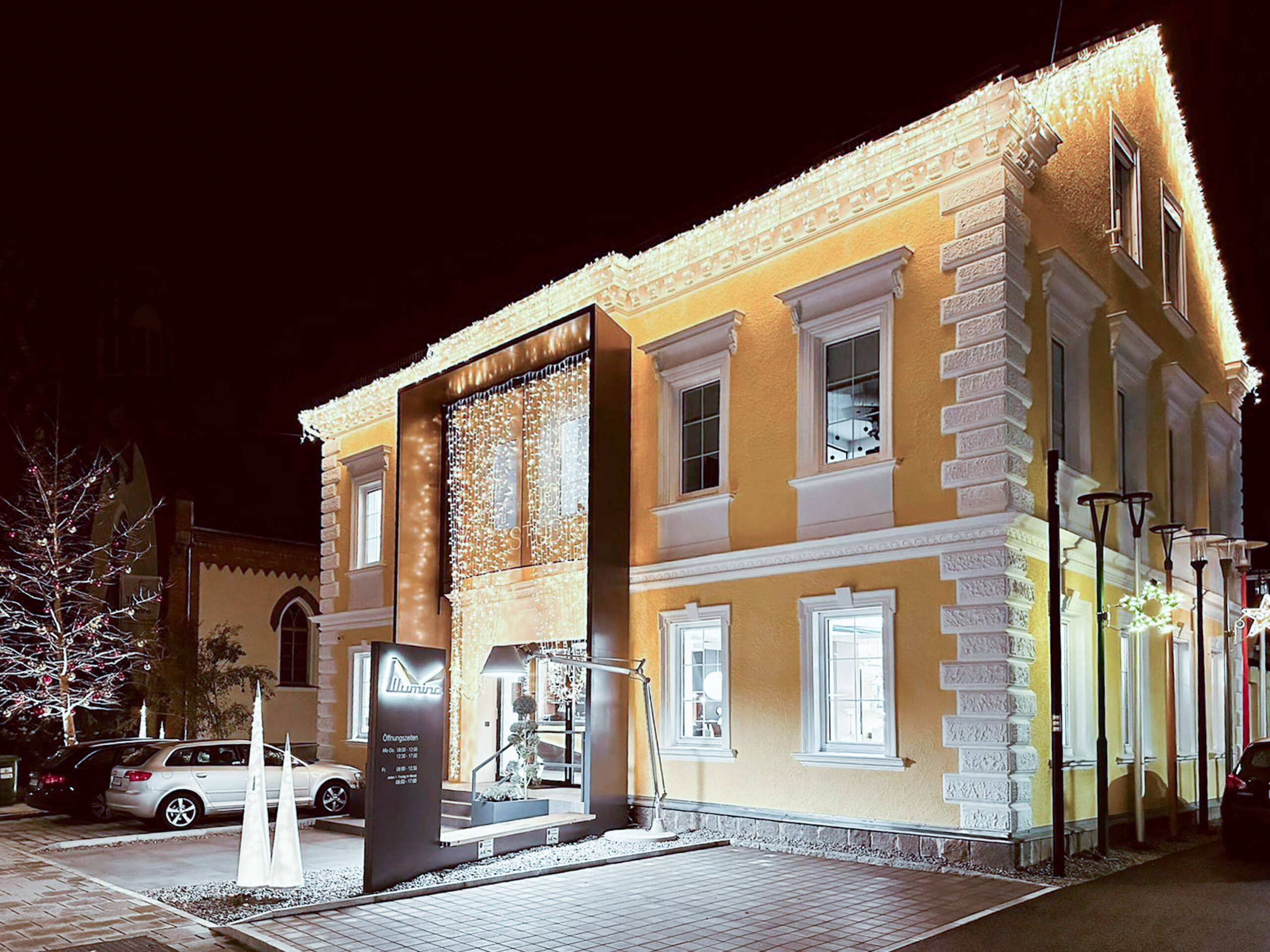 Gelbes Gebäude mit Lichtplanung von Illumina, beleuchtete Fassade und Bäume in der Nacht