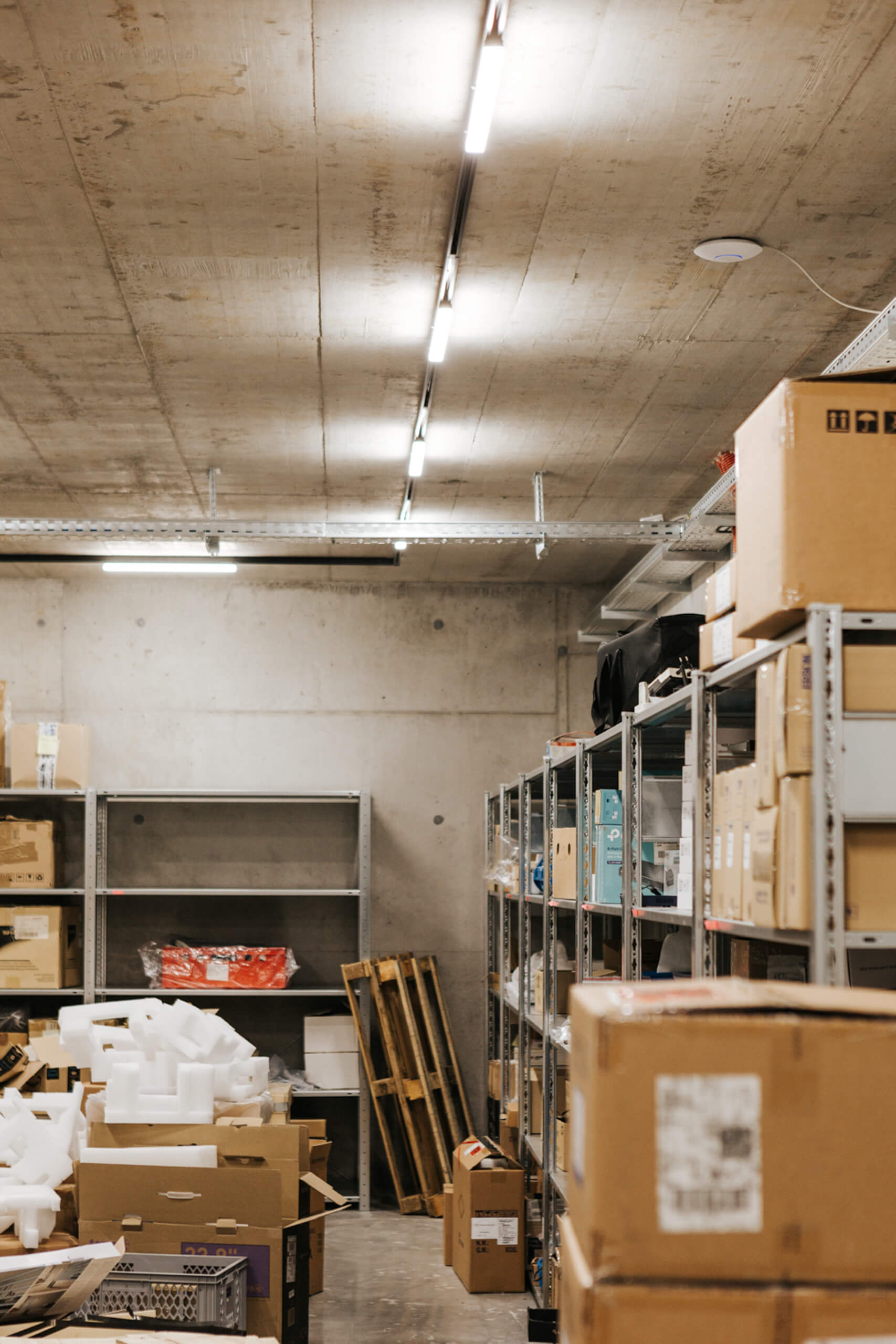 Lagerhalle mit Regalen, Kartons und Paletten, beleuchtet durch moderne Hallenleuchten.